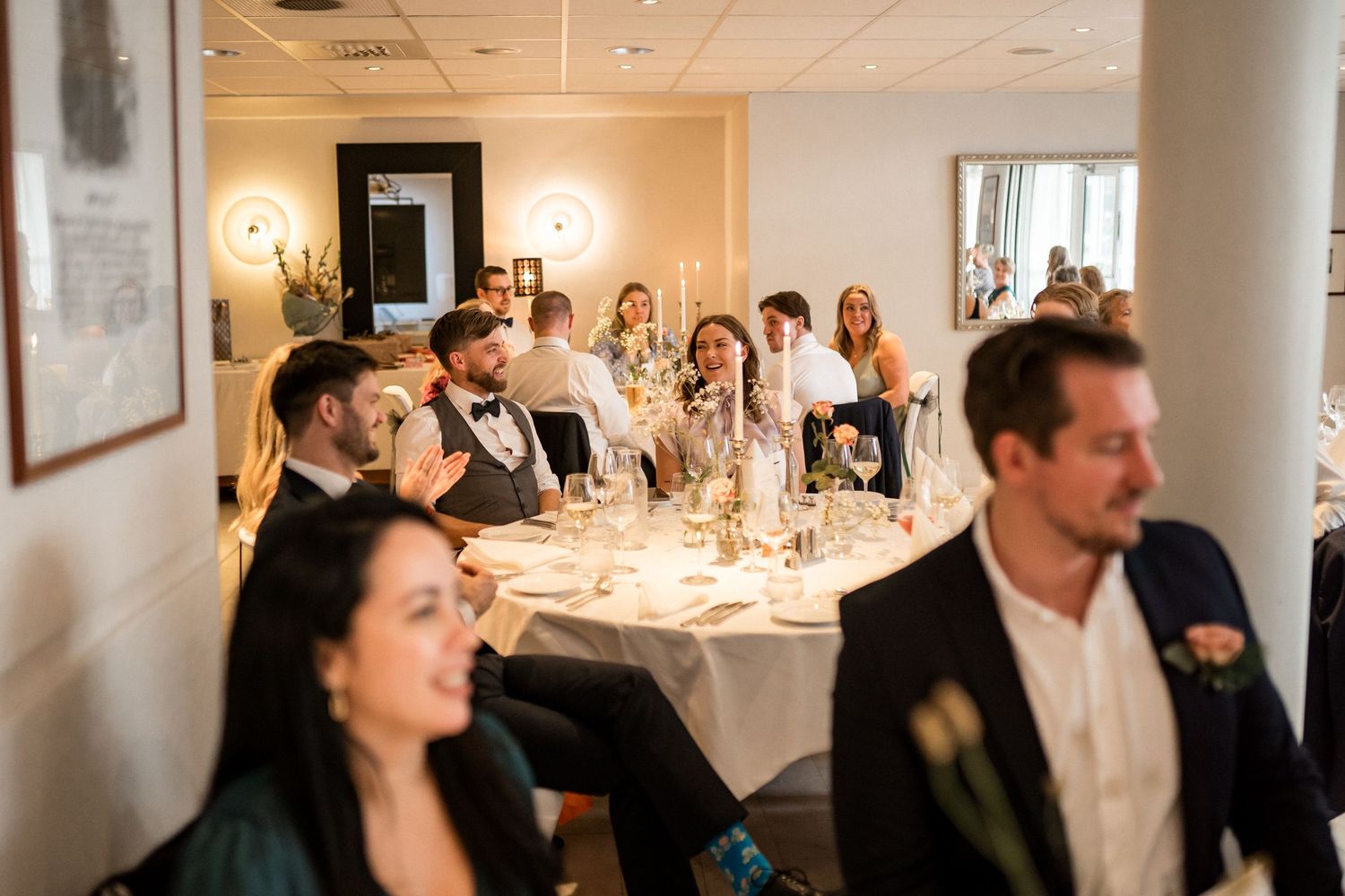 Wedding reception dining room with guests seated at tables under warm lighting.