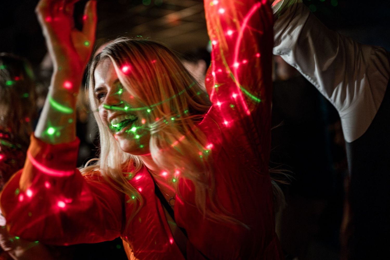 Red and green string lights create romantic ambiance on dark dance floor at wedding reception.