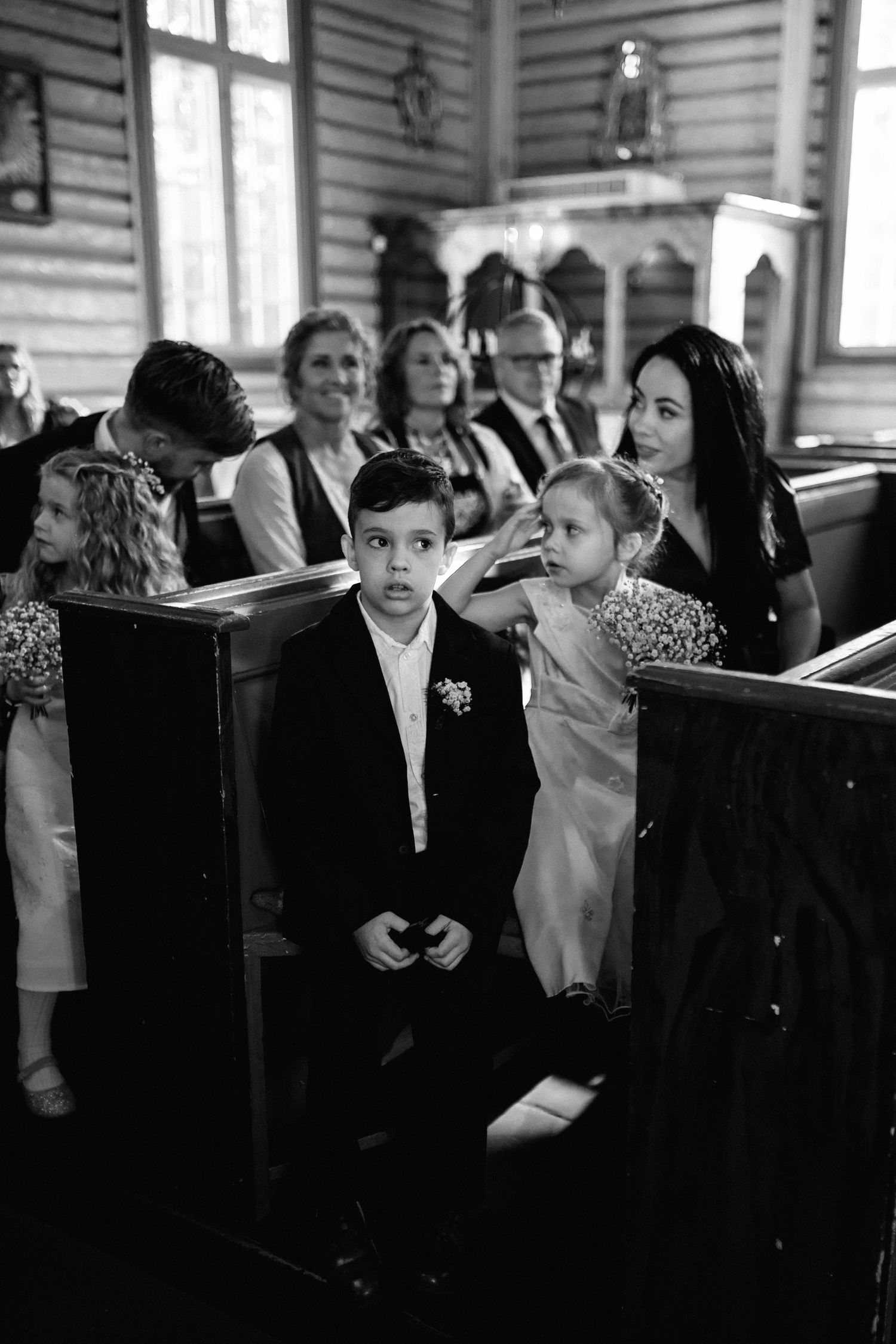 Black and white photo of wedding guests seated in wooden church pews.