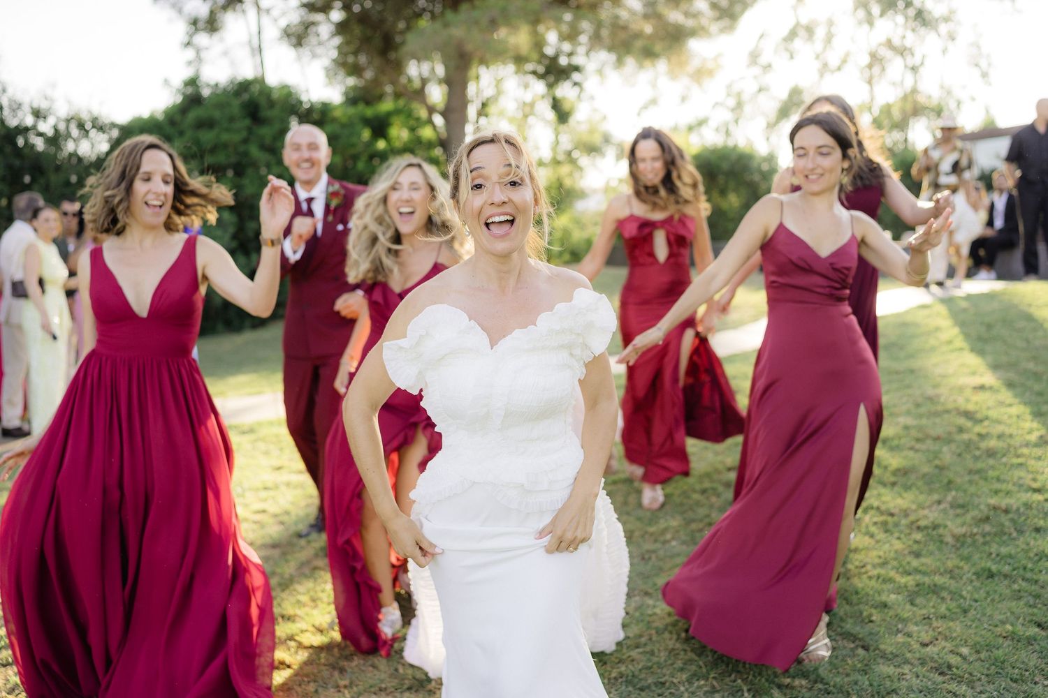 Wedding party in burgundy dresses posing with the bride outdoors.
