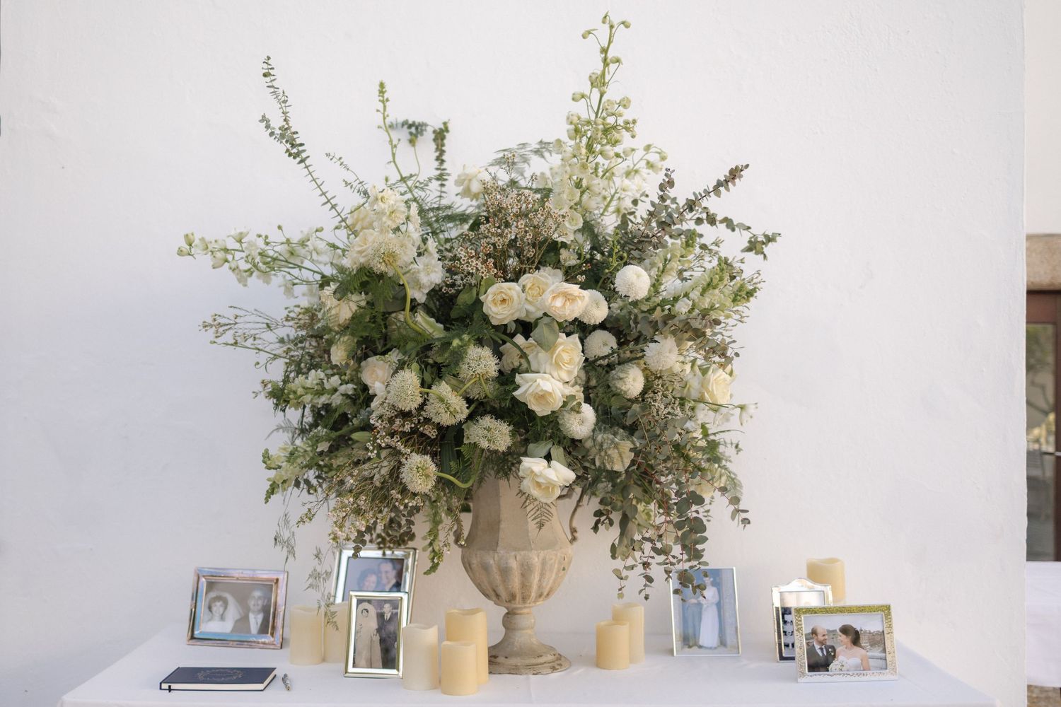 Elegant white floral arrangement with candles and framed photographs on display.