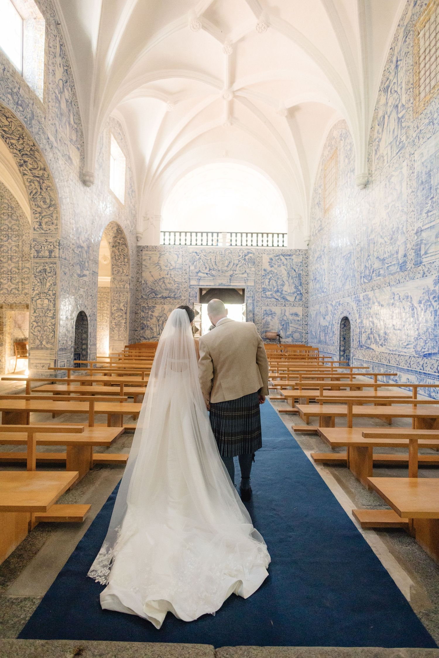 Church interior with blue azulejo tiles and wooden pews along a navy blue carpet aisle.