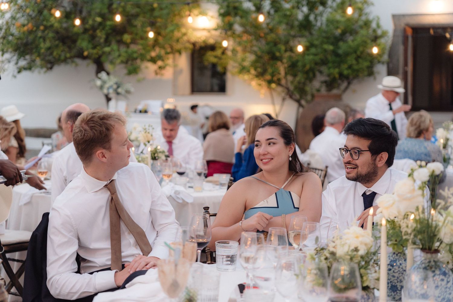 Guests dining at decorated tables under string lights at an outdoor evening celebration.