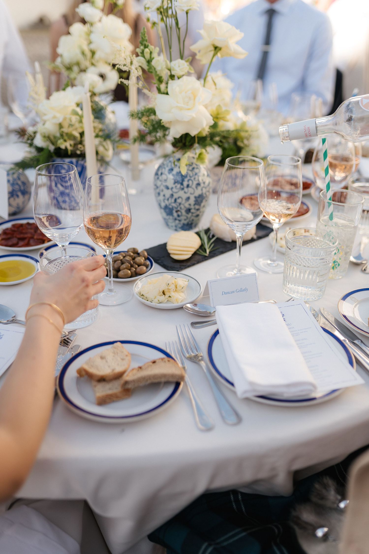 Elegant table settings with white floral centerpieces and blue accents at a formal outdoor dinner.