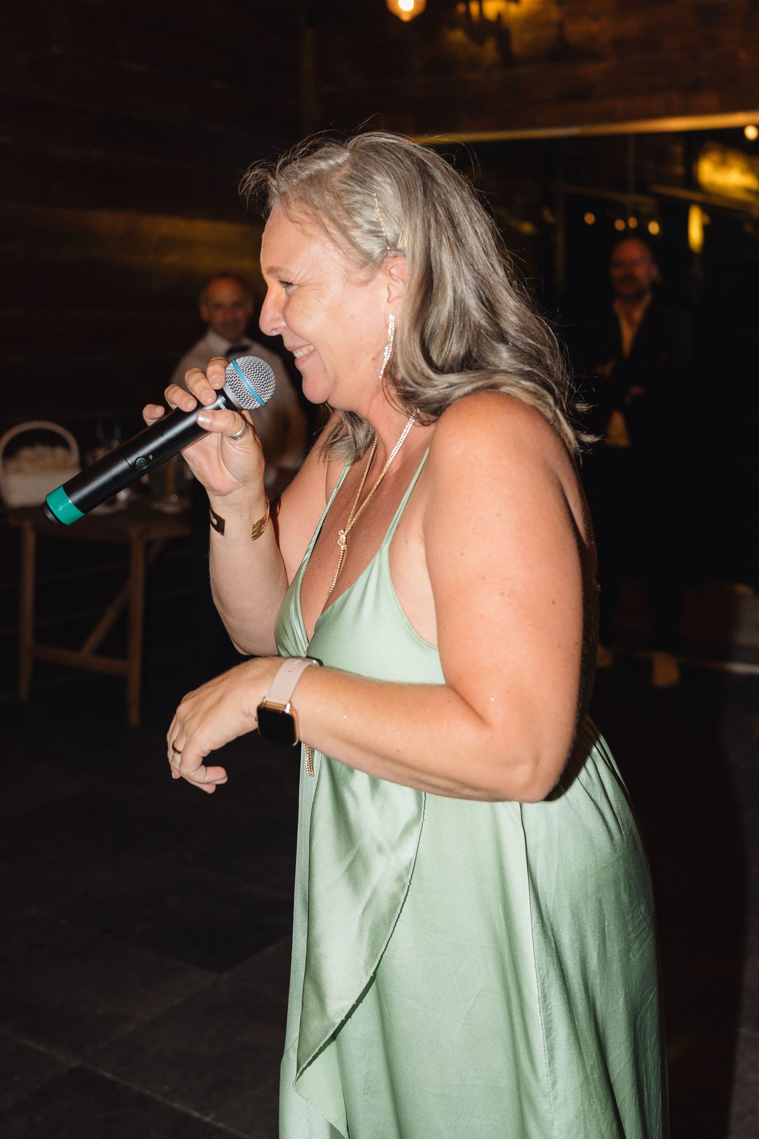 A performer in a mint green dress sings with a microphone at an evening event.