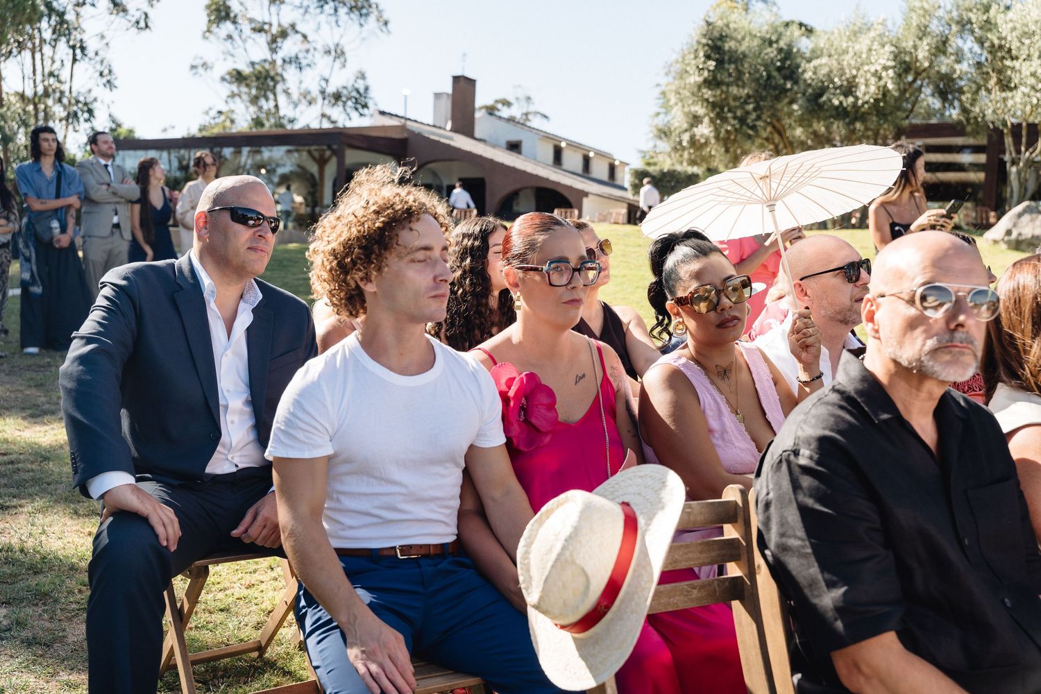 Outdoor wedding ceremony guests react emotionally while seated in wooden chairs.