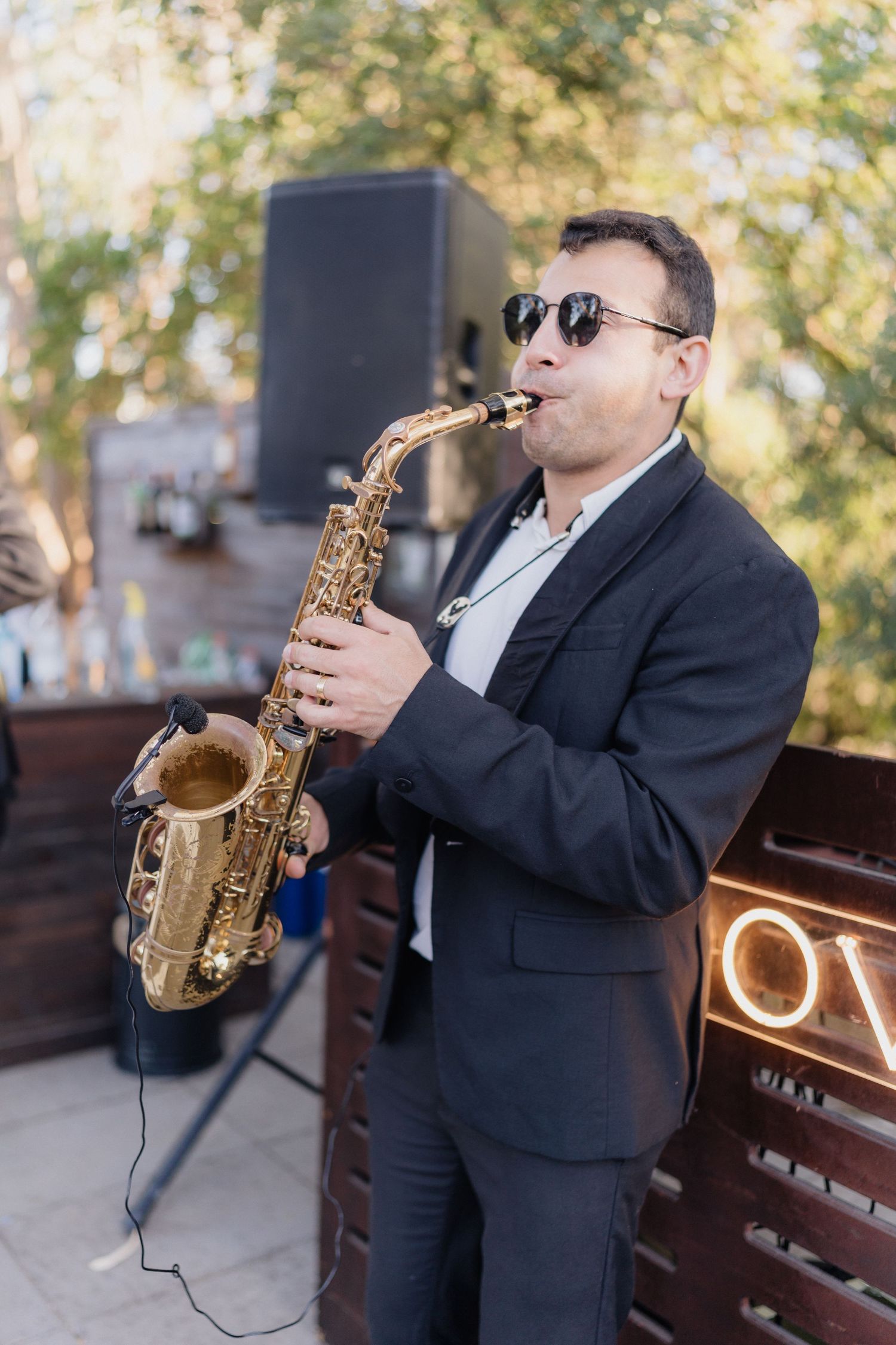 Saxophone player in a black suit performing music outdoors.