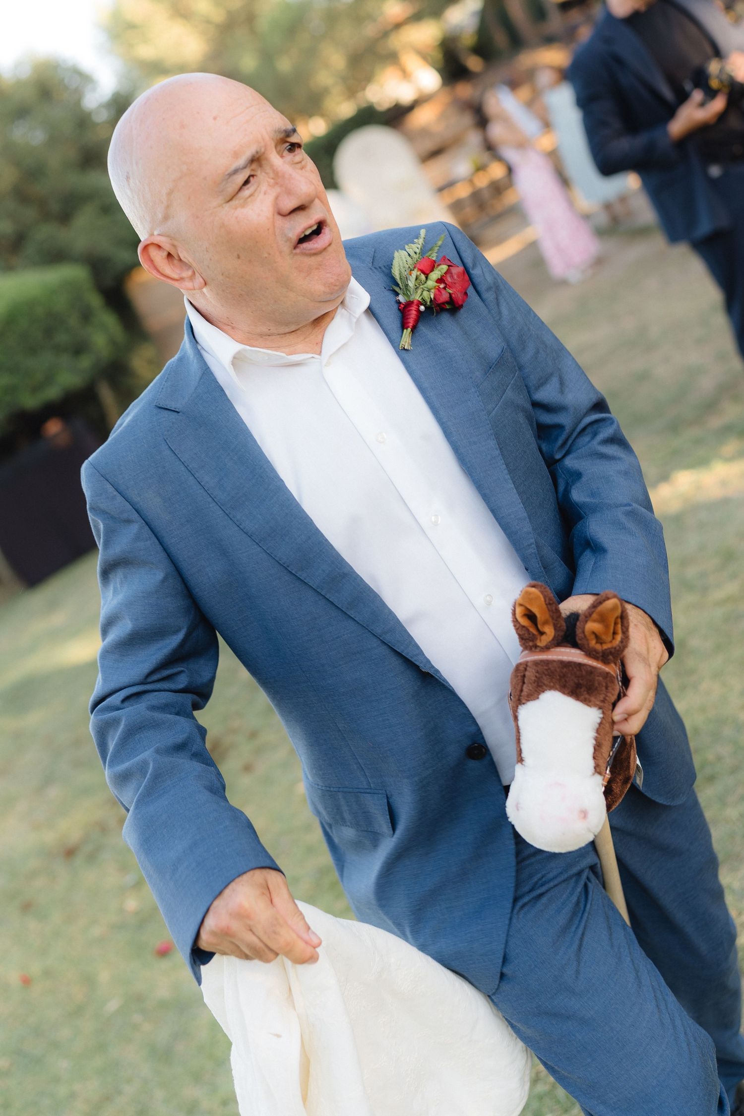 A guest in a blue suit laughs during an outdoor wedding celebration.