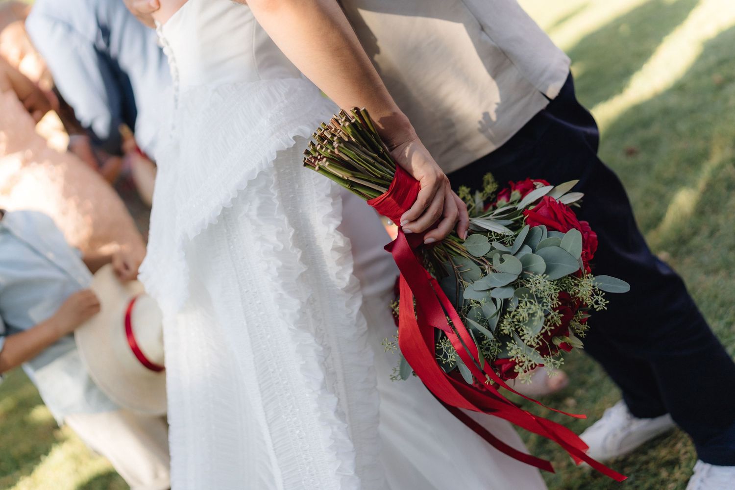 Wedding guests share emotional embraces while holding red floral bouquets.