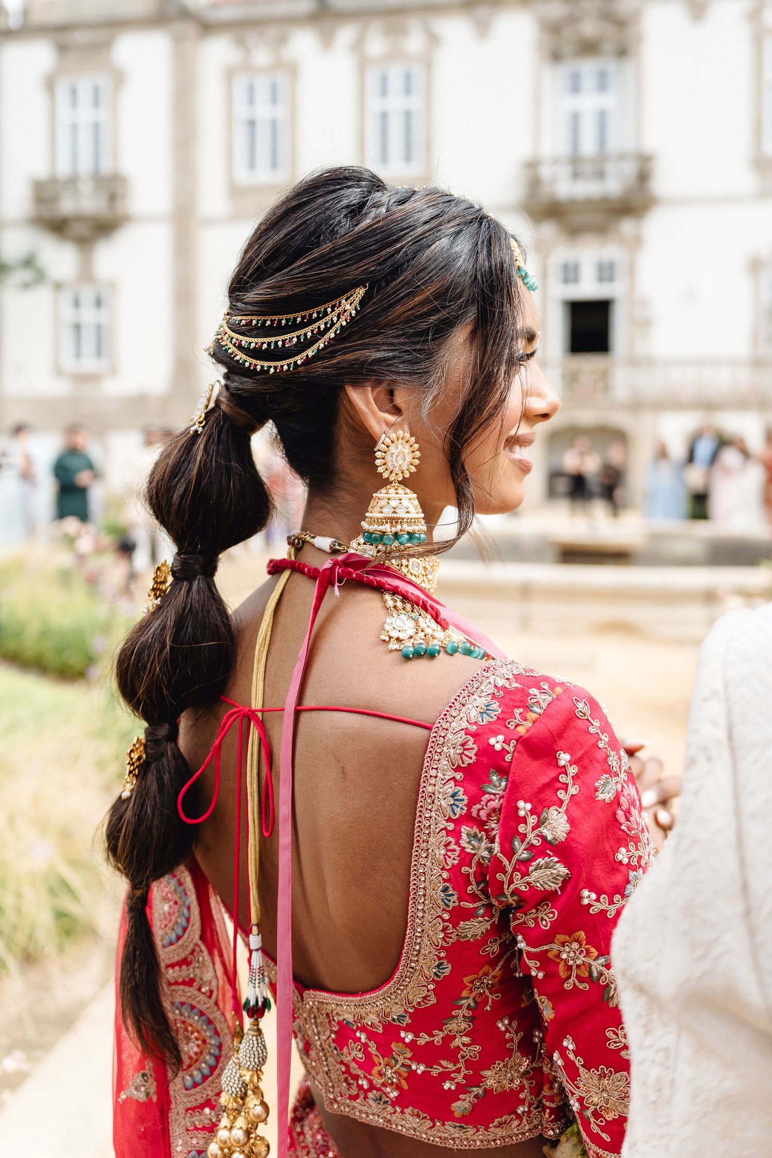 Back view of bride in red lehenga showing intricate hair jewelry and embroidered details.