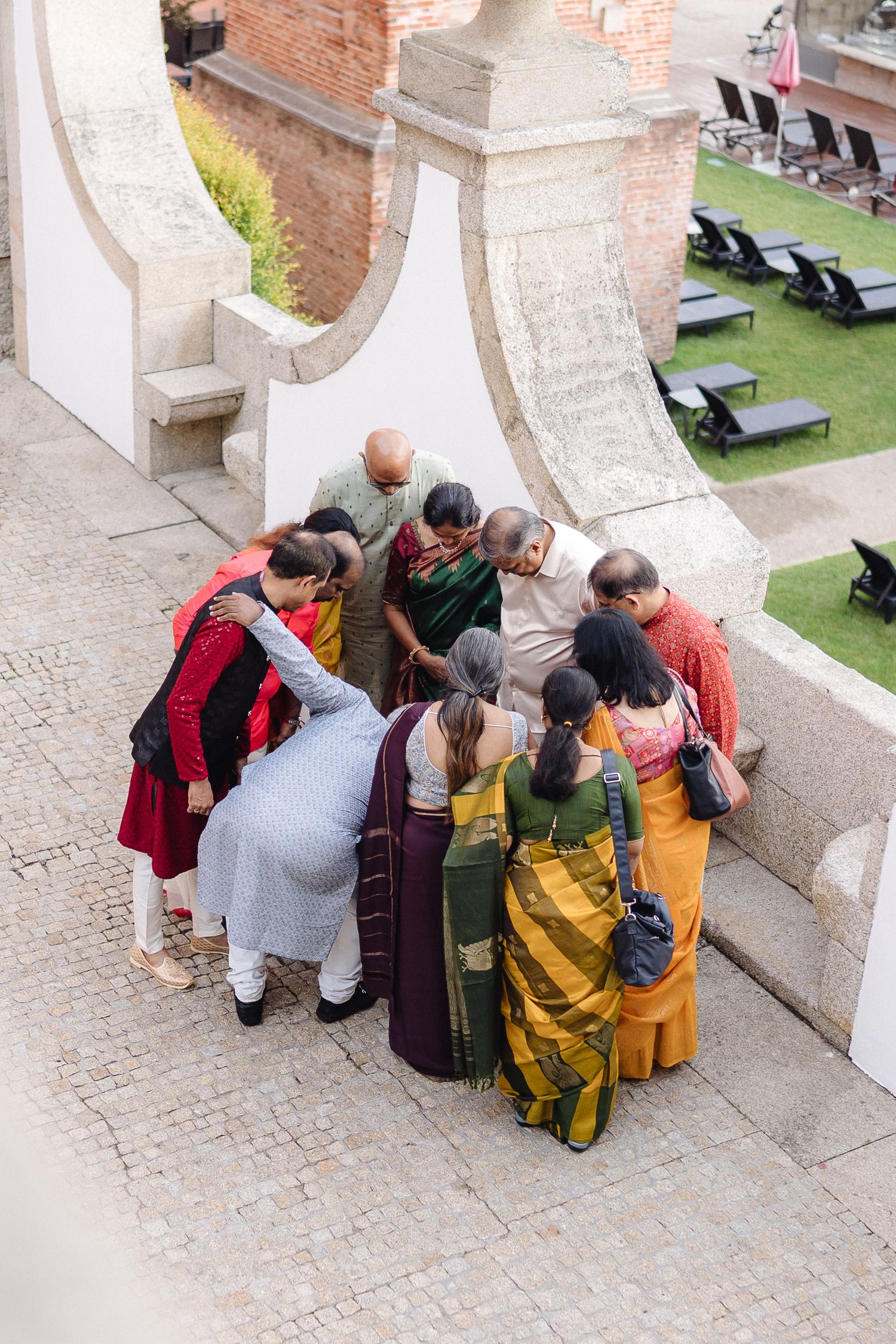 Group photo session on stone steps at an elegant outdoor venue with guests in colorful attire.