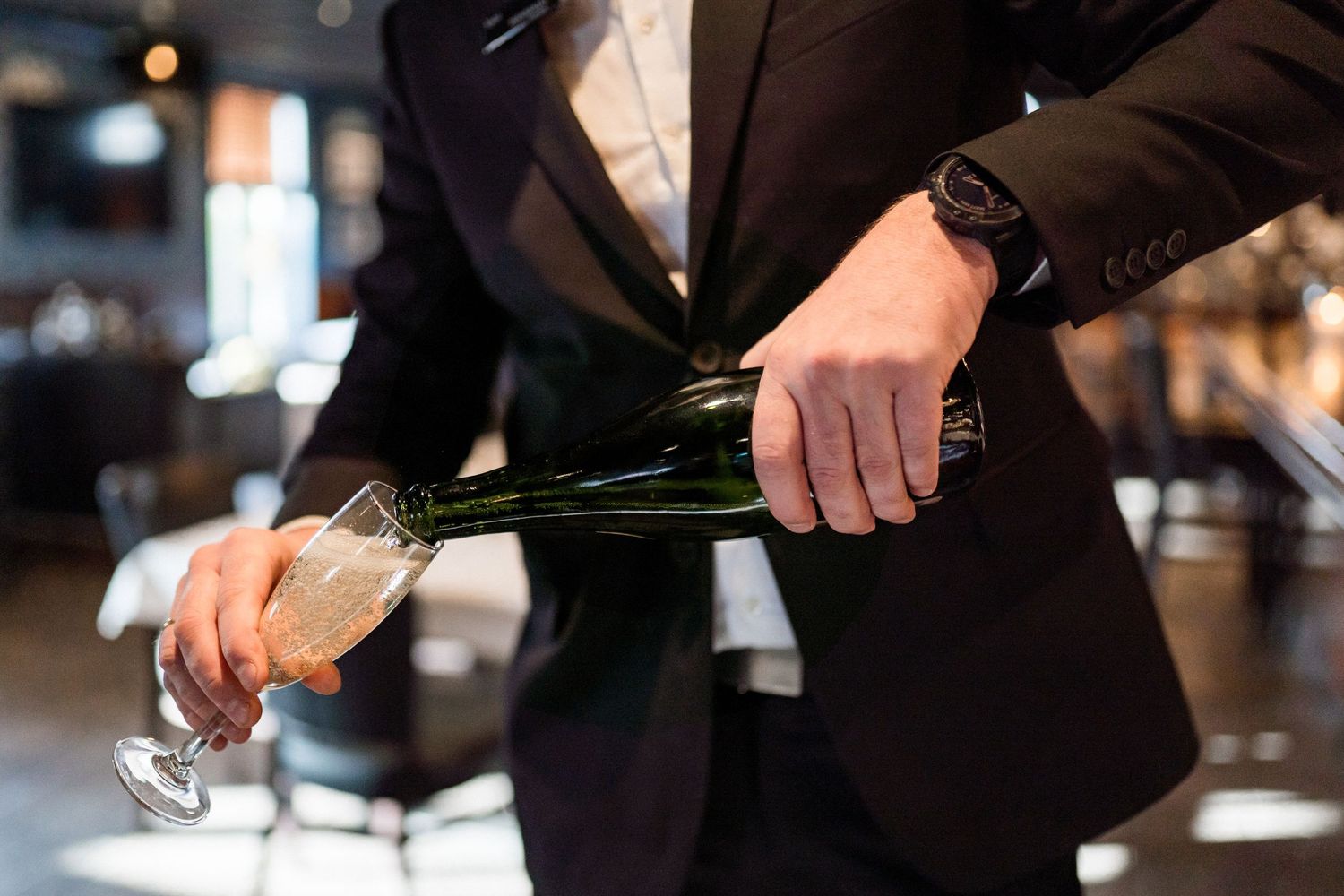 Hands pouring champagne into glasses at formal event.
