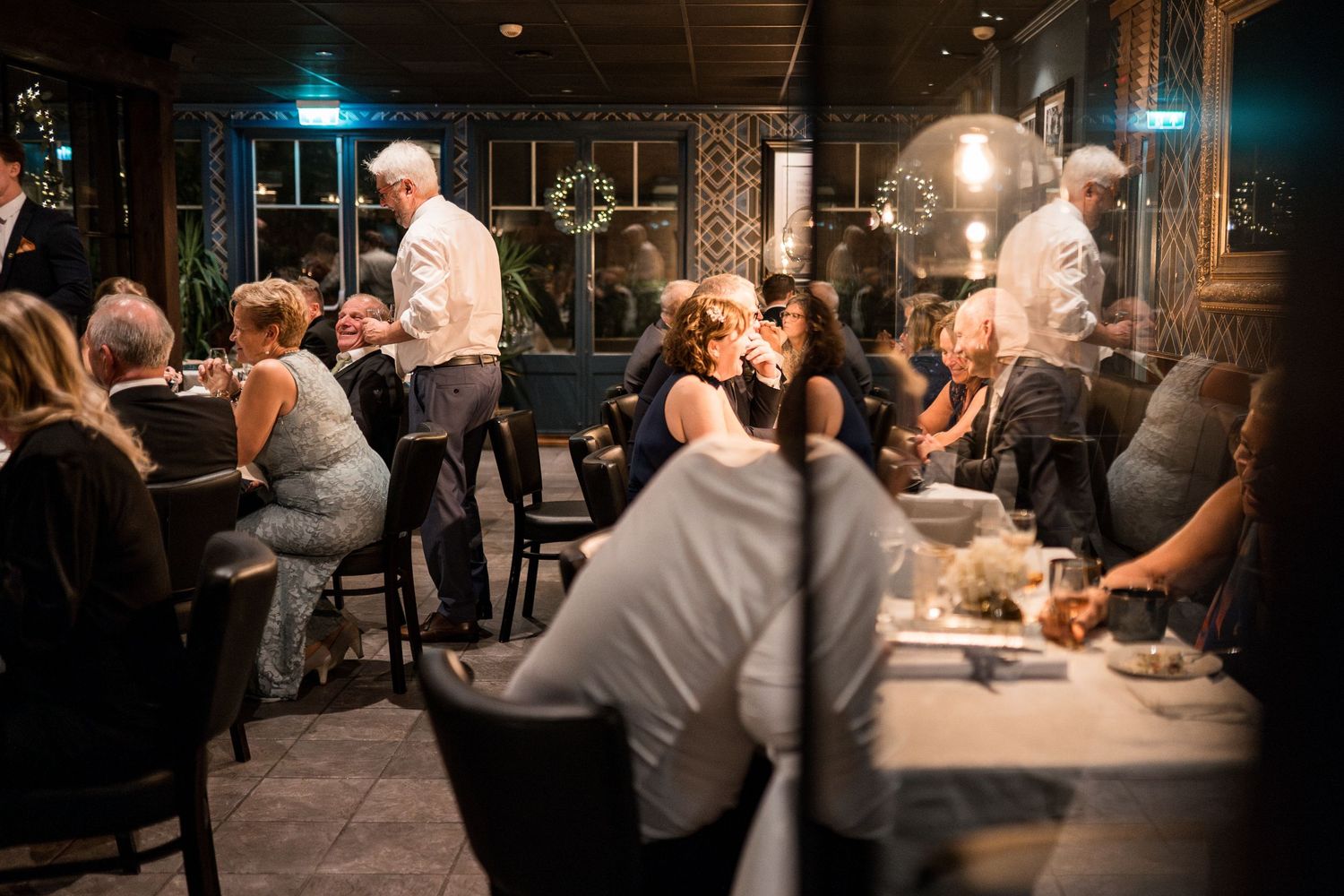 Dimly lit reception venue with guests gathered around tables creating an intimate atmosphere.