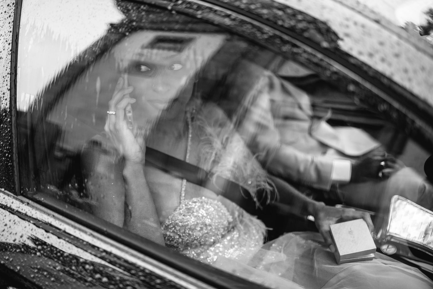 Raindrops on car windshield creating abstract patterns in black and white.