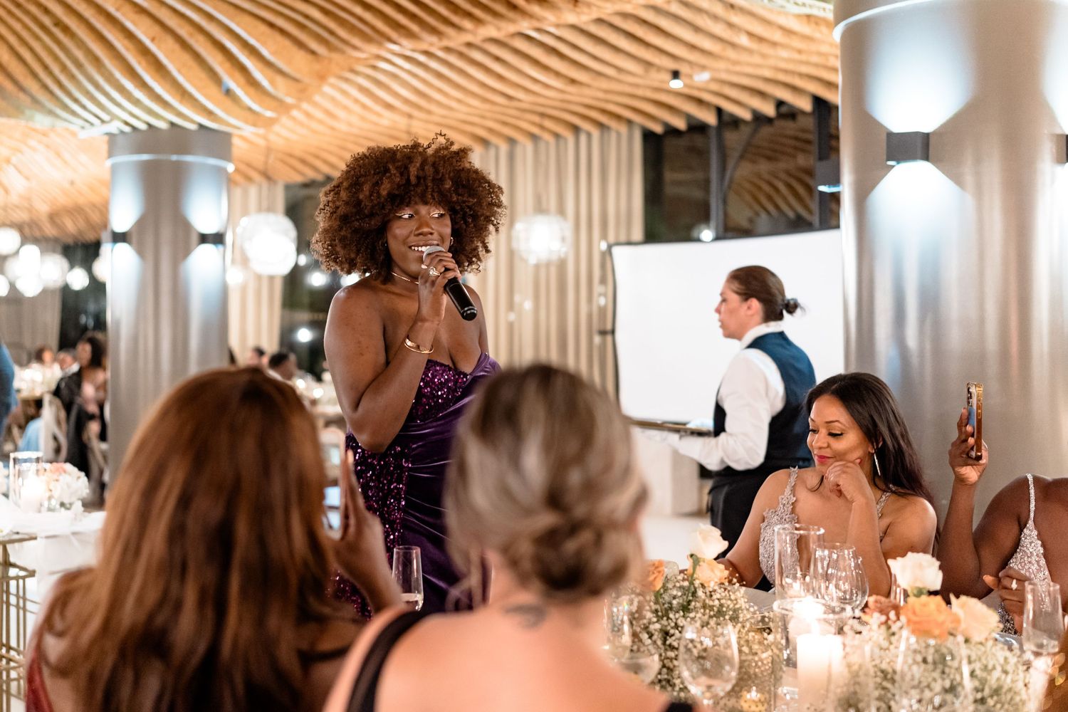 Wedding reception guests mingle and celebrate at decorated indoor venue tables.