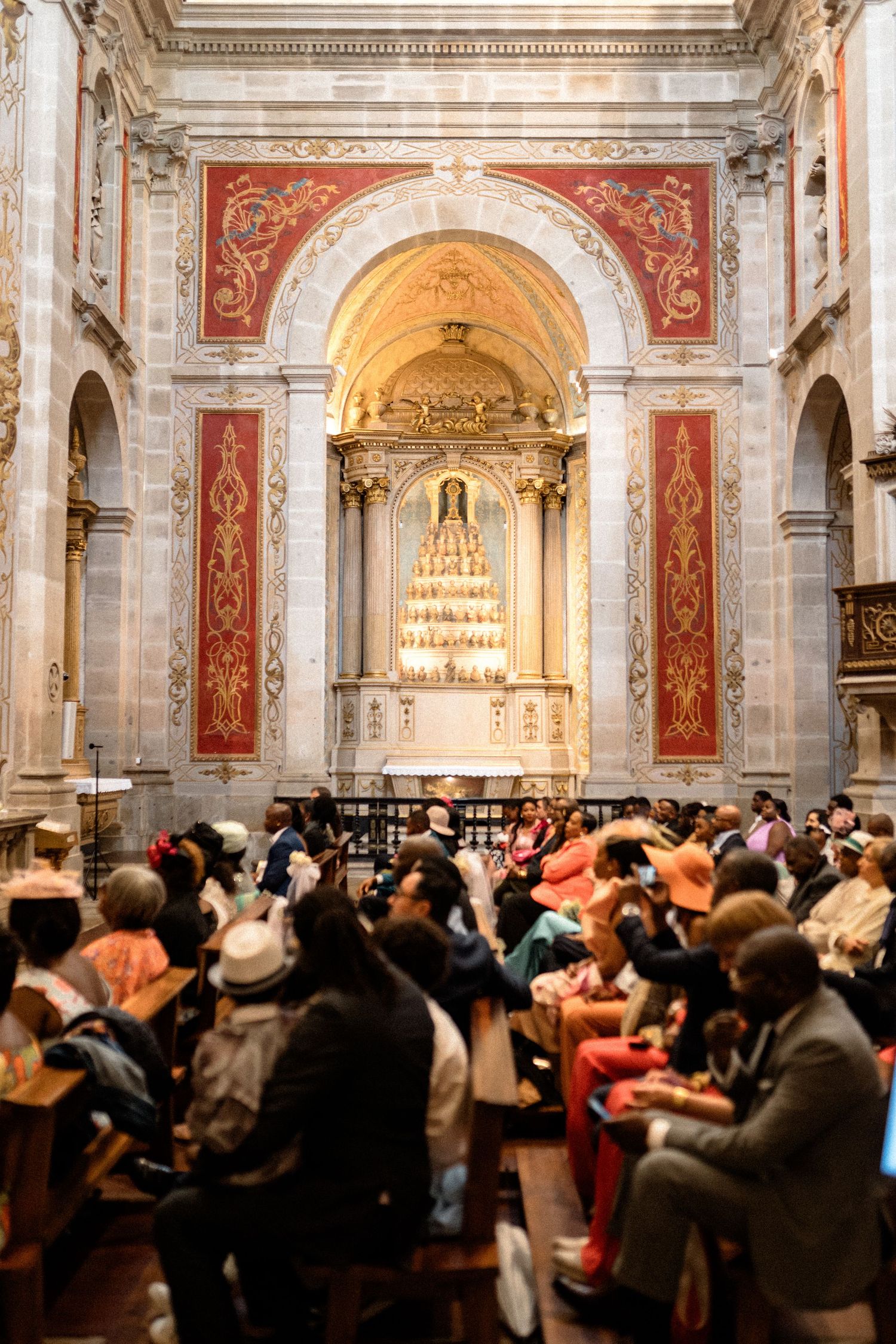 Large crowd gathered inside a historic cathedral with ornate red and gold architectural details.