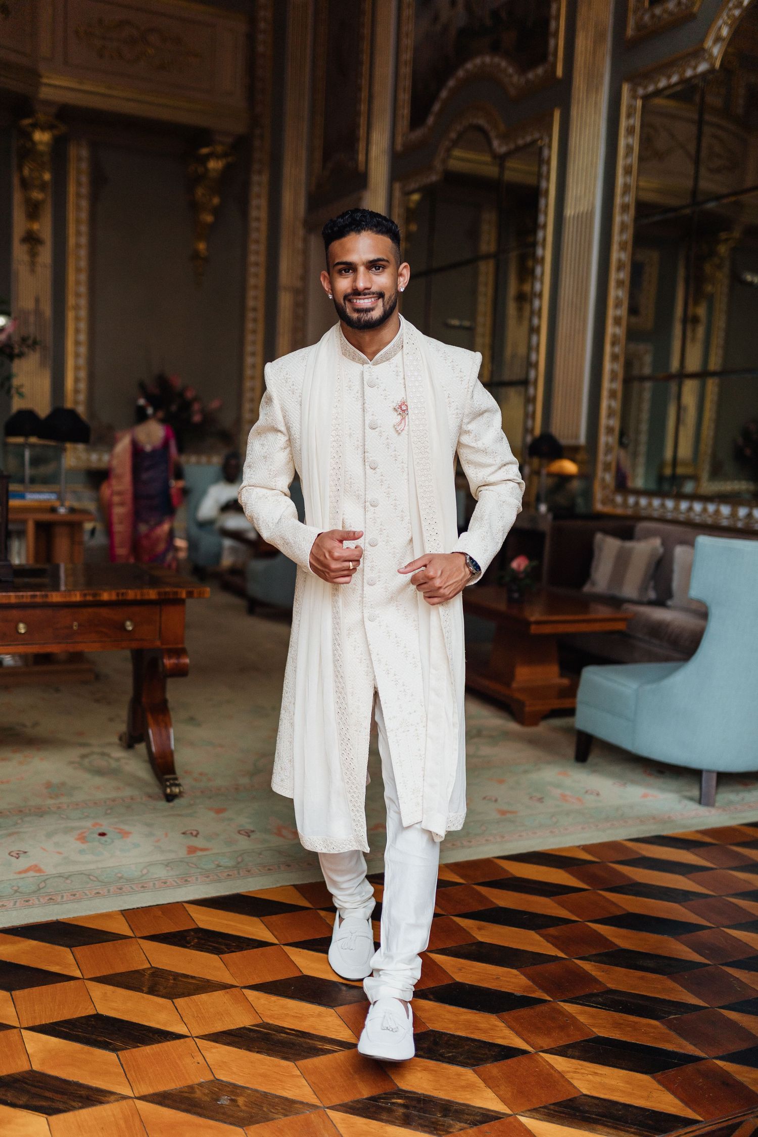 Elegant white traditional Indian groom's outfit showcased on ornate patterned floor.