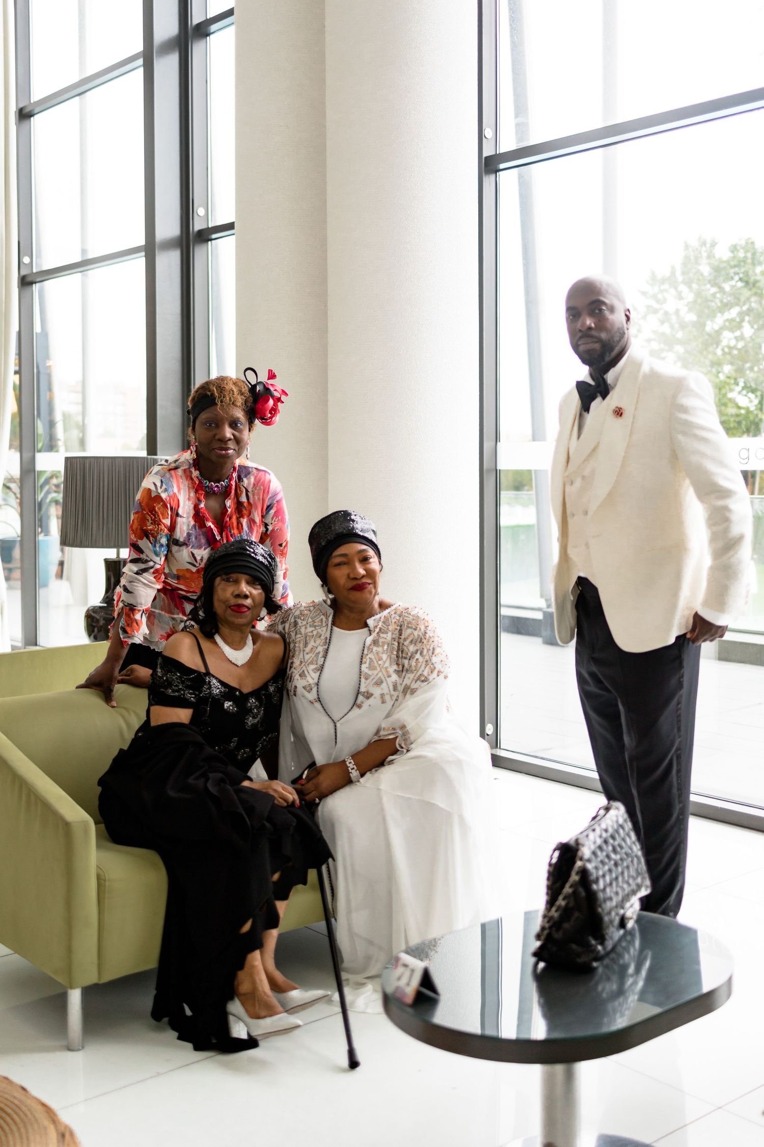 A formal group photo in a modern space with large windows, featuring elegant attire and a green couch.