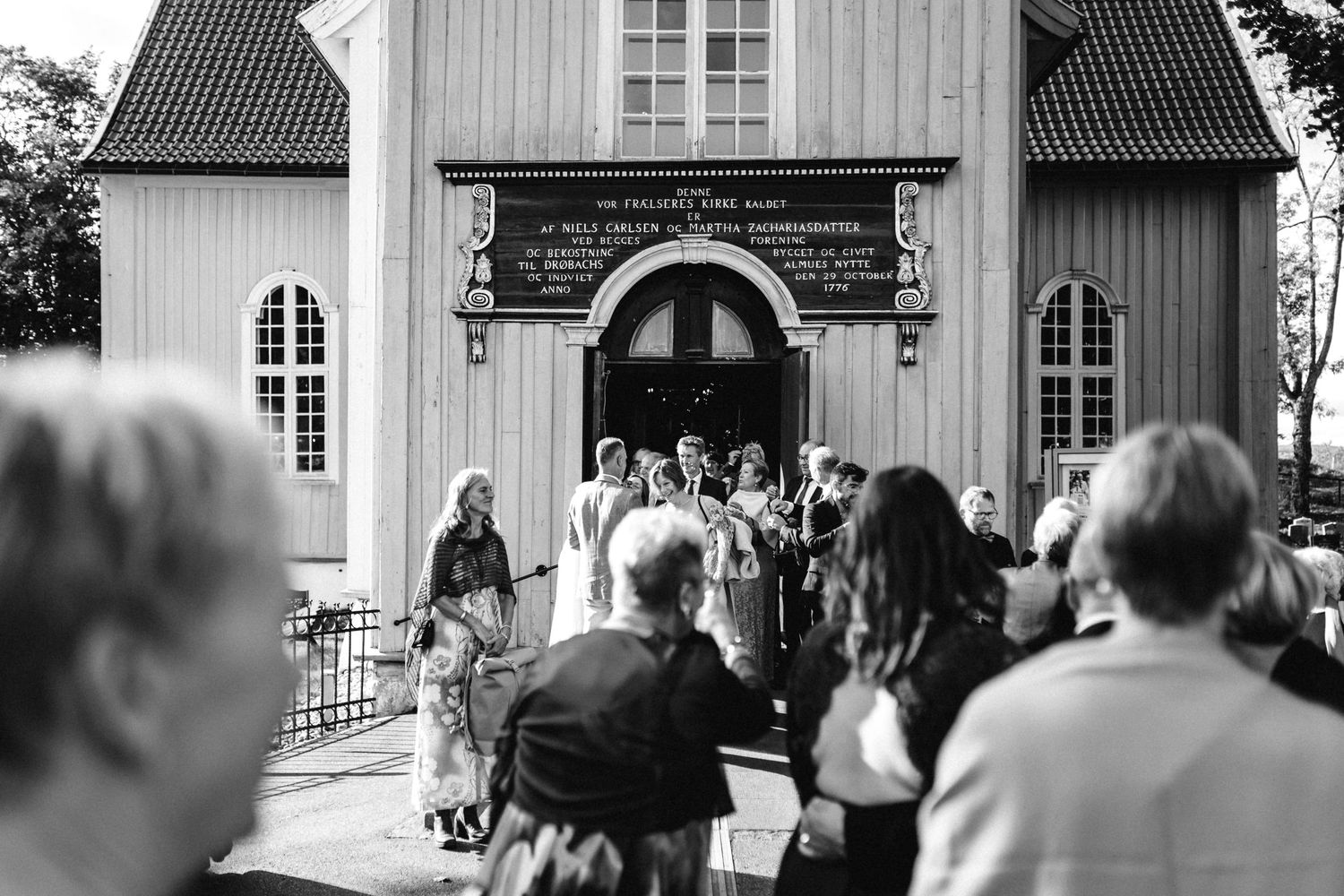 Exterior view of a traditional white church with guests gathering for a wedding ceremony.