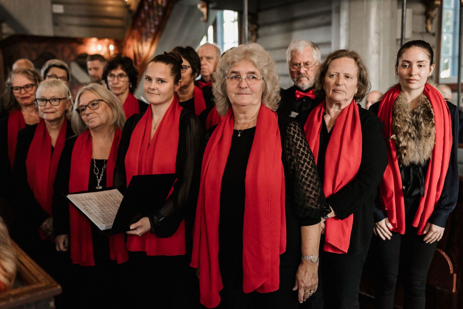 Group photo of choir members wearing black outfits with bright red scarves.