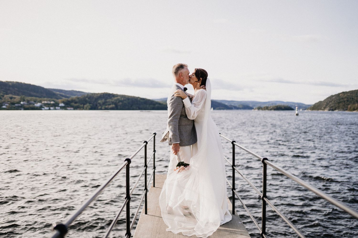 Wedding photography sequence on a waterfront dock with mountains and lake in the background.