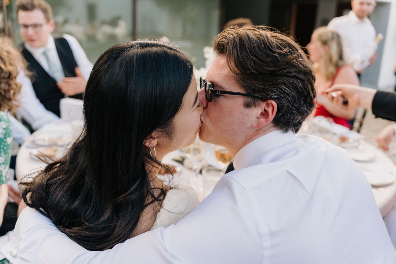 Wedding guests enjoying an outdoor celebration with drinks and laughter at a sunny venue.
