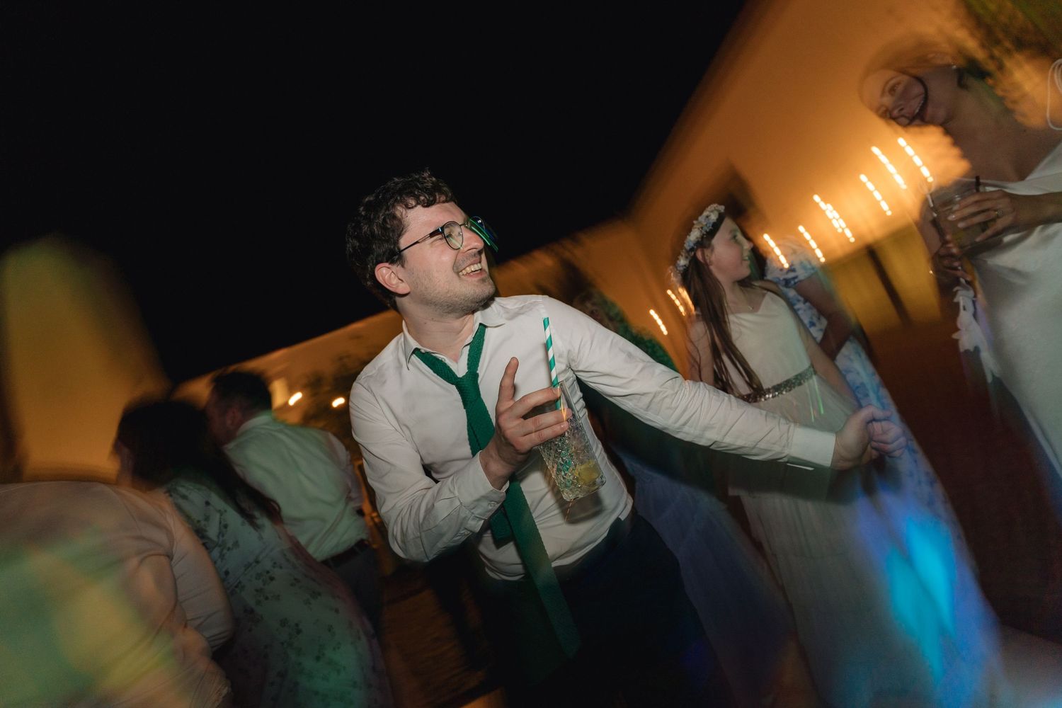 People dancing and celebrating at a dimly lit party with colorful lighting effects.