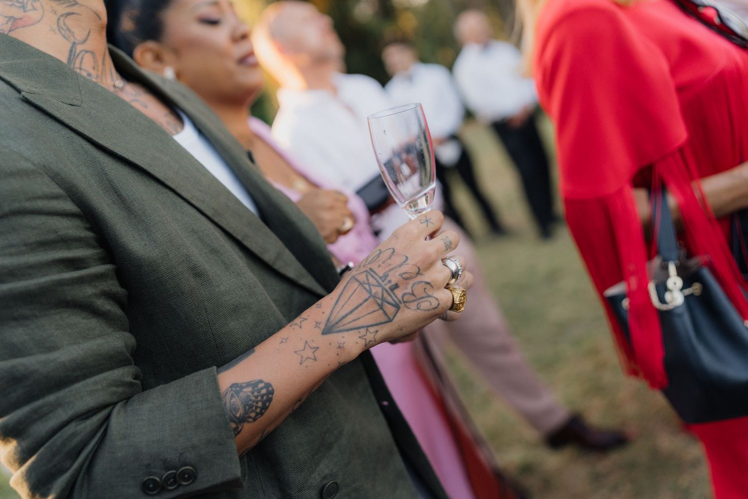Wedding guests with tattoos enjoying drinks at outdoor celebration.