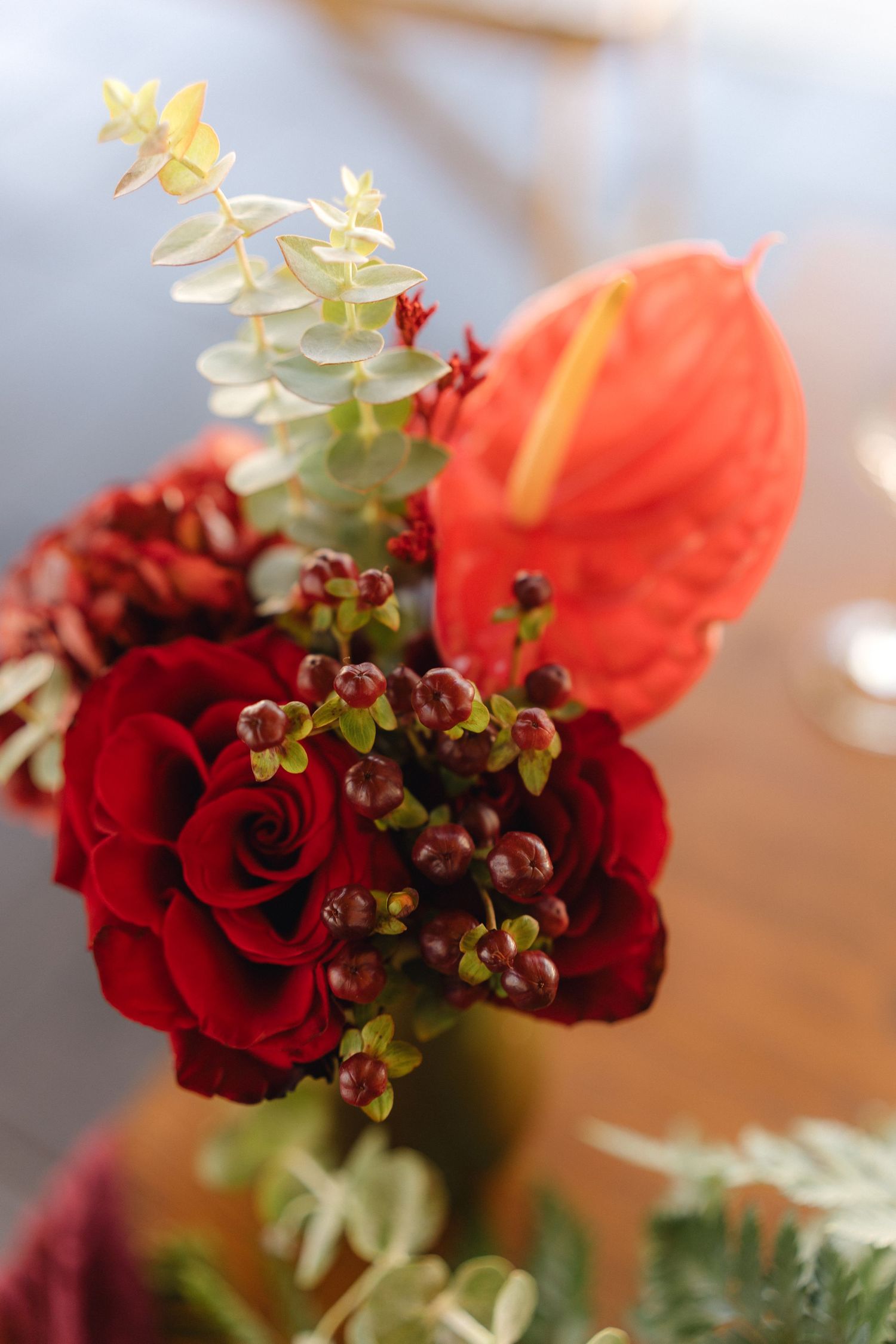 Vibrant red roses and coral flowers arranged with greenery in an artistic centerpiece.