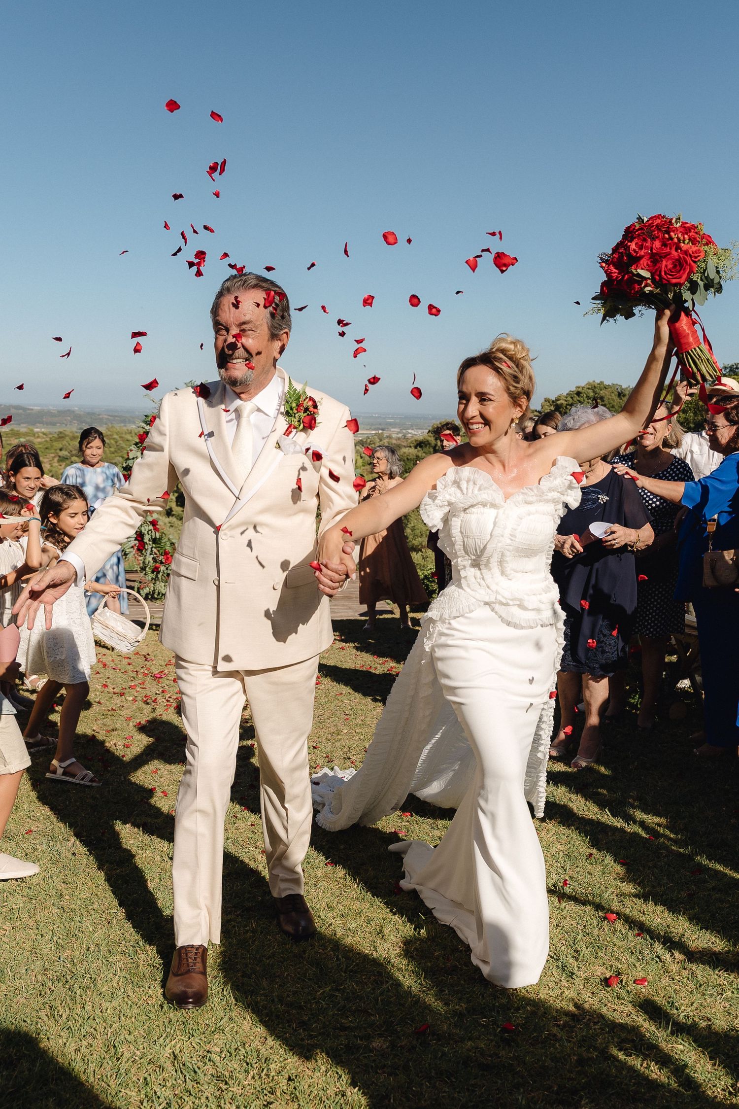 Wedding couple and guests celebrate with red rose petals being tossed in the air.