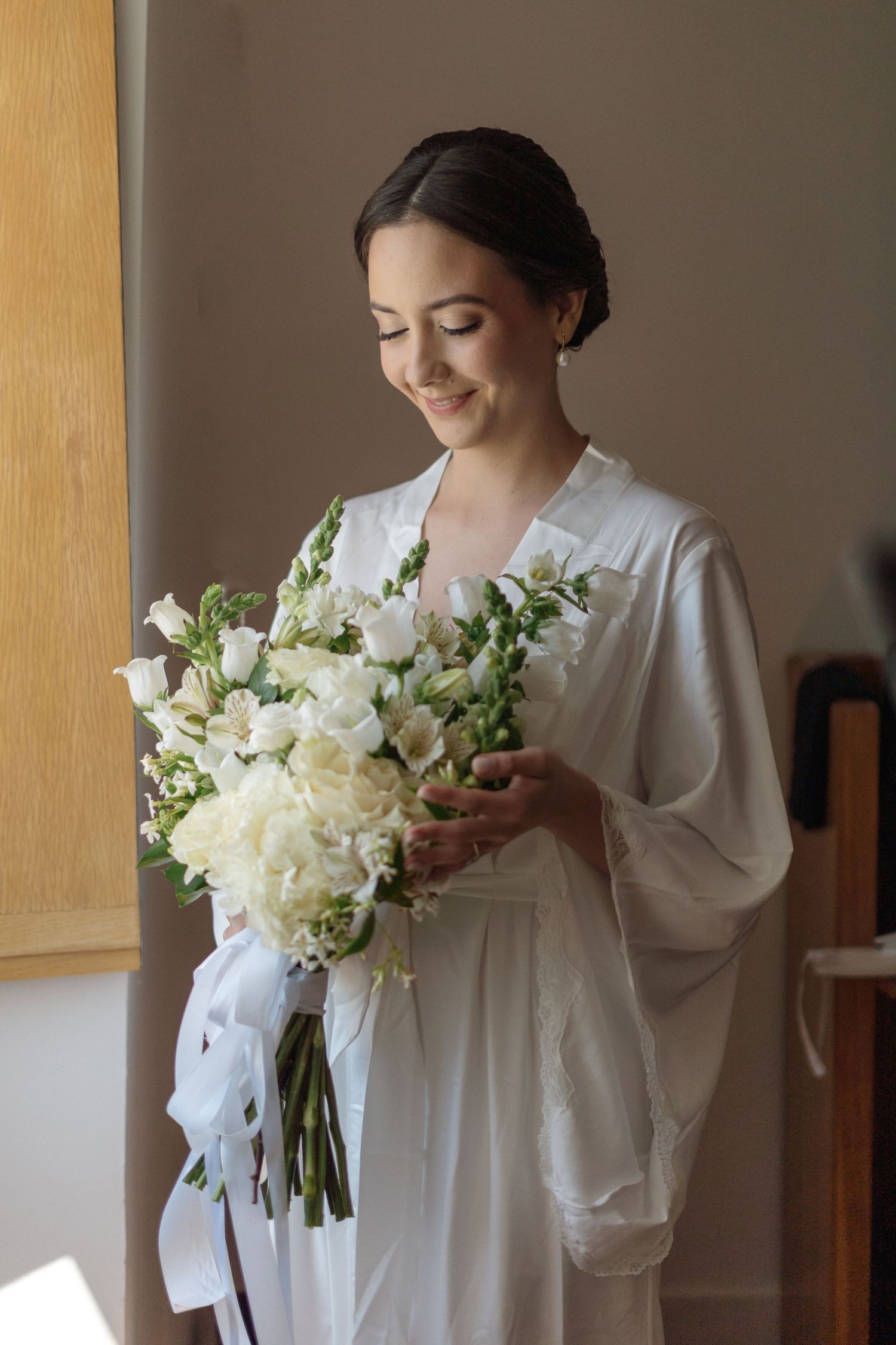 Person in white robe holding elegant white floral bouquet during wedding preparations.