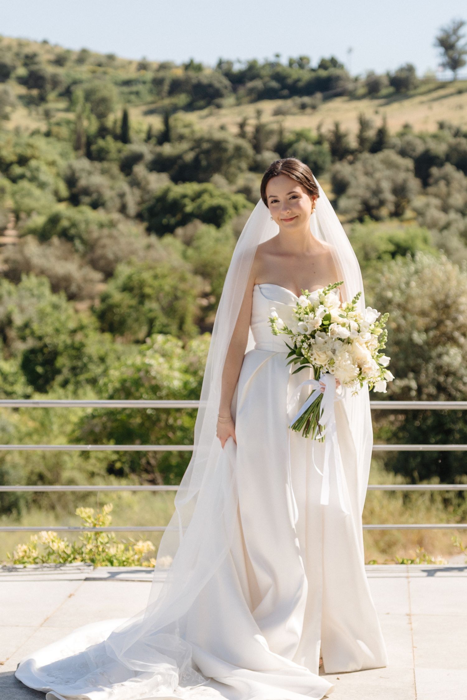 Classic bridal portrait with white bouquet against scenic hillside landscape.
