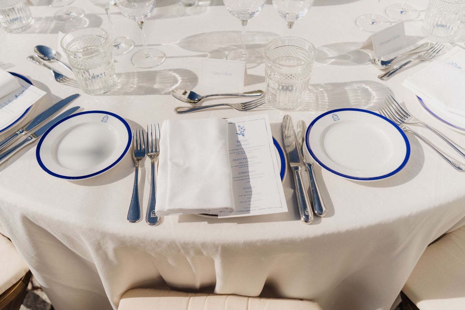 Formal place settings with white plates trimmed in blue and polished silverware on crisp white tablecloths.