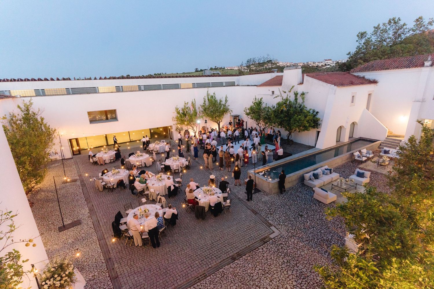 Aerial view of outdoor wedding reception with white tables and chairs arranged in courtyard.