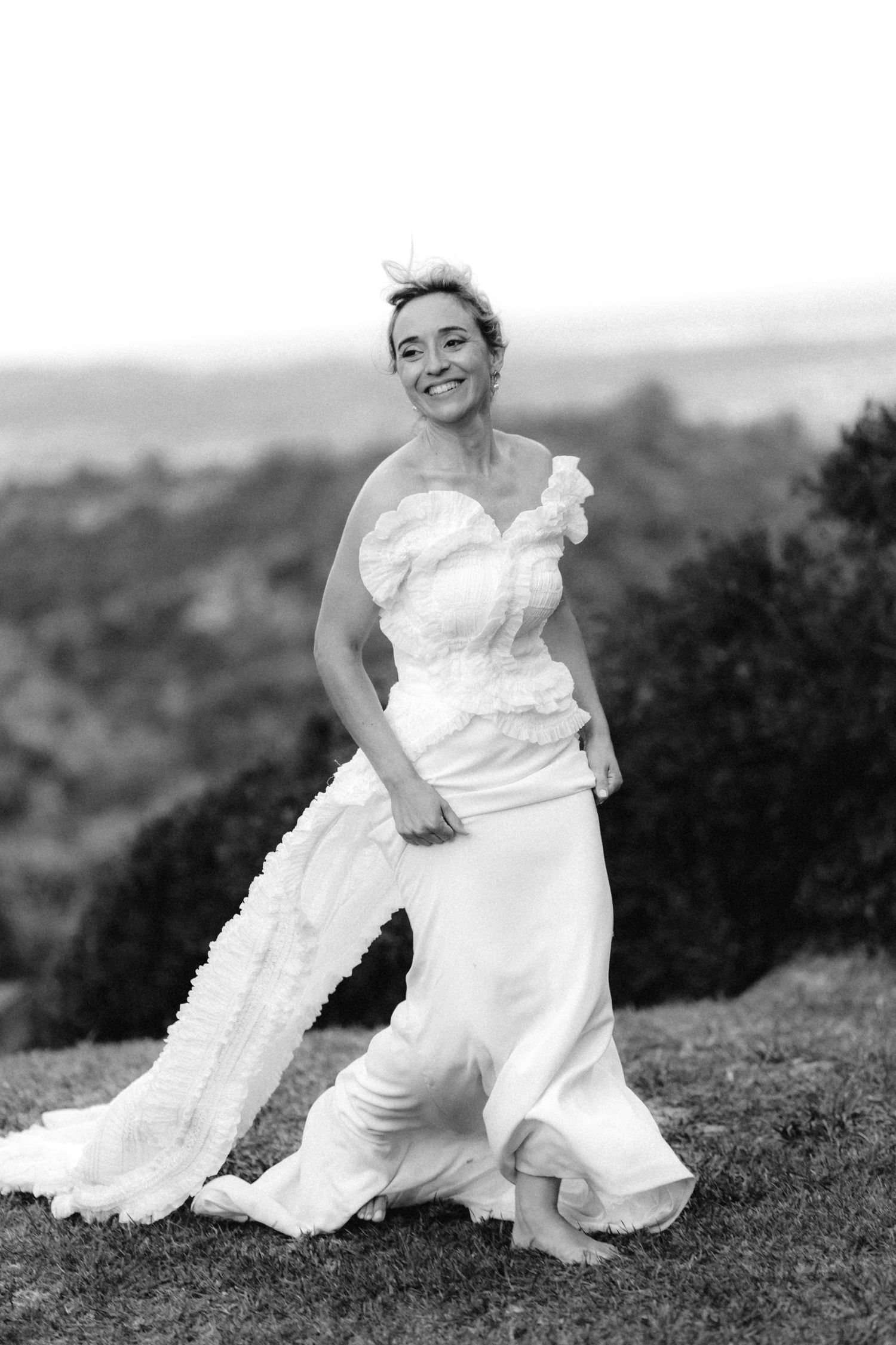 Black and white photos show bride twirling in flowing white wedding dress on grassy hill.