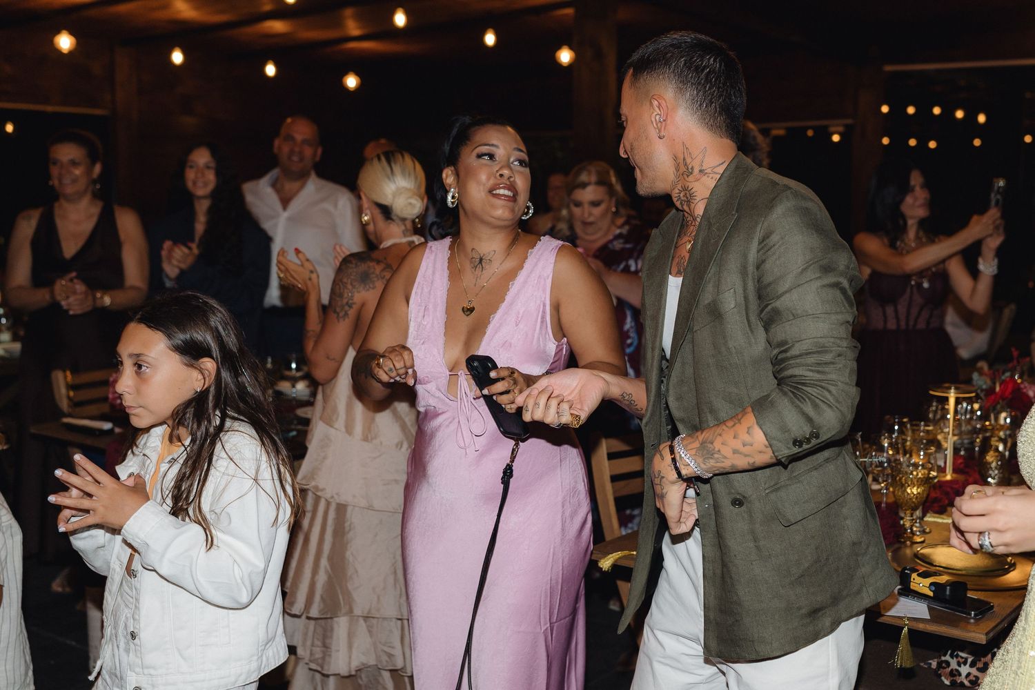 Wedding reception guests dancing and celebrating under warm lighting at an evening party.