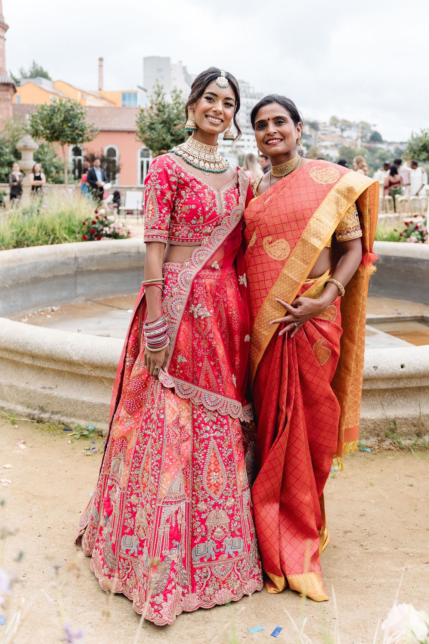 Wedding party members in red and gold traditional Indian attire pose outdoors.