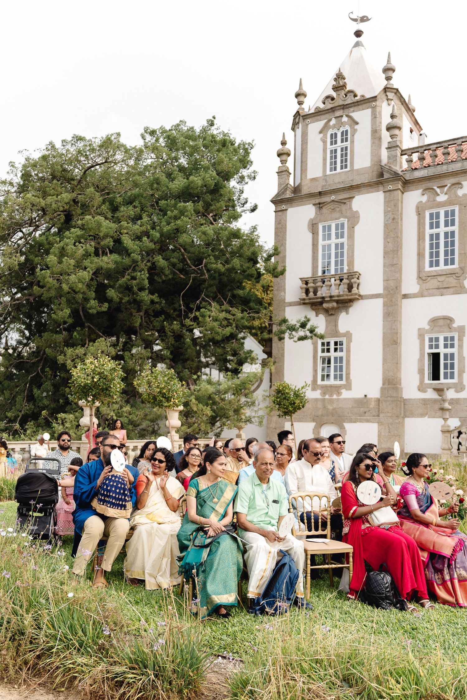 Large group of wedding guests gathered outside a grand historic building with white facade.