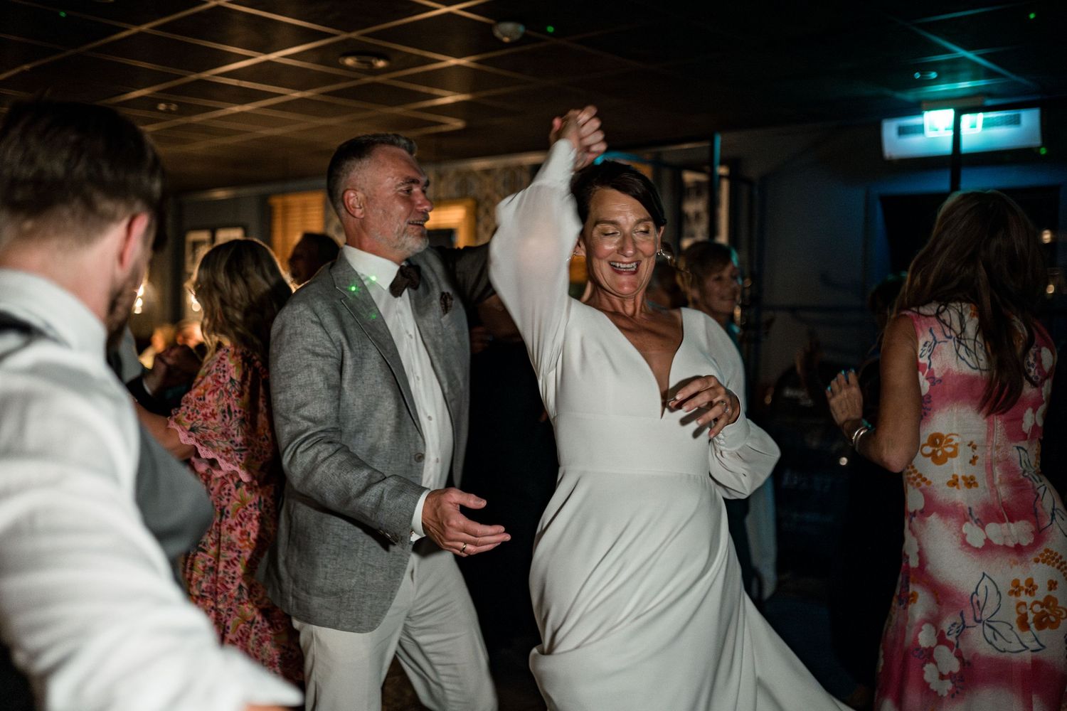 Wedding guests dancing and celebrating on a dimly lit dance floor at reception.