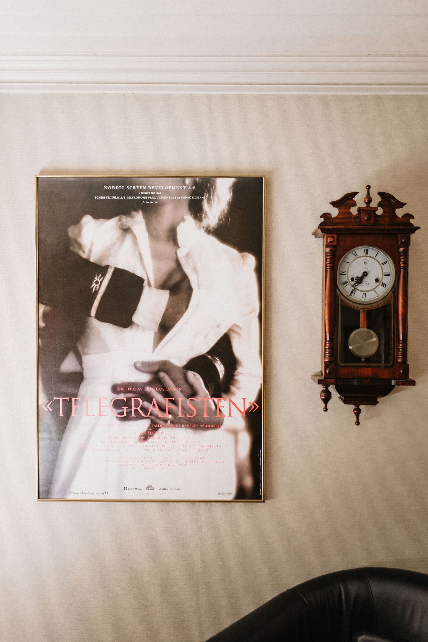 A black and white fashion poster hangs on a beige wall next to an ornate wooden pendulum clock.