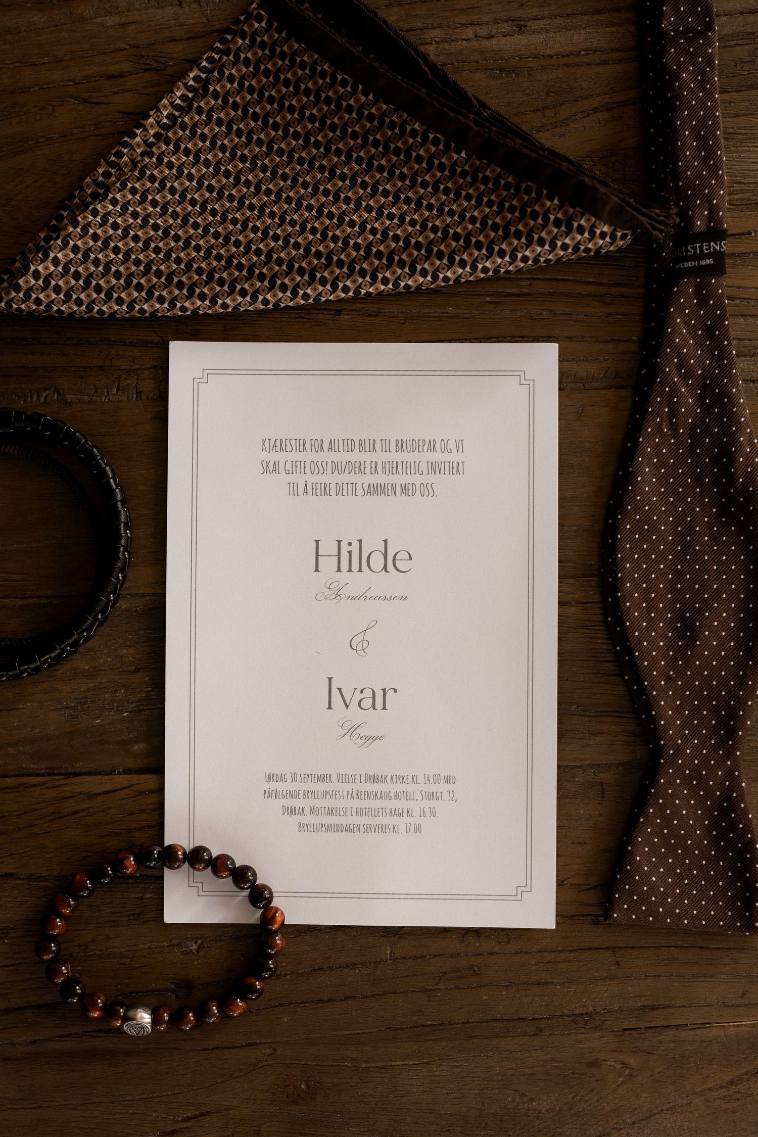 Wedding invitation cards with names displayed on dark wooden surface with decorative elements.