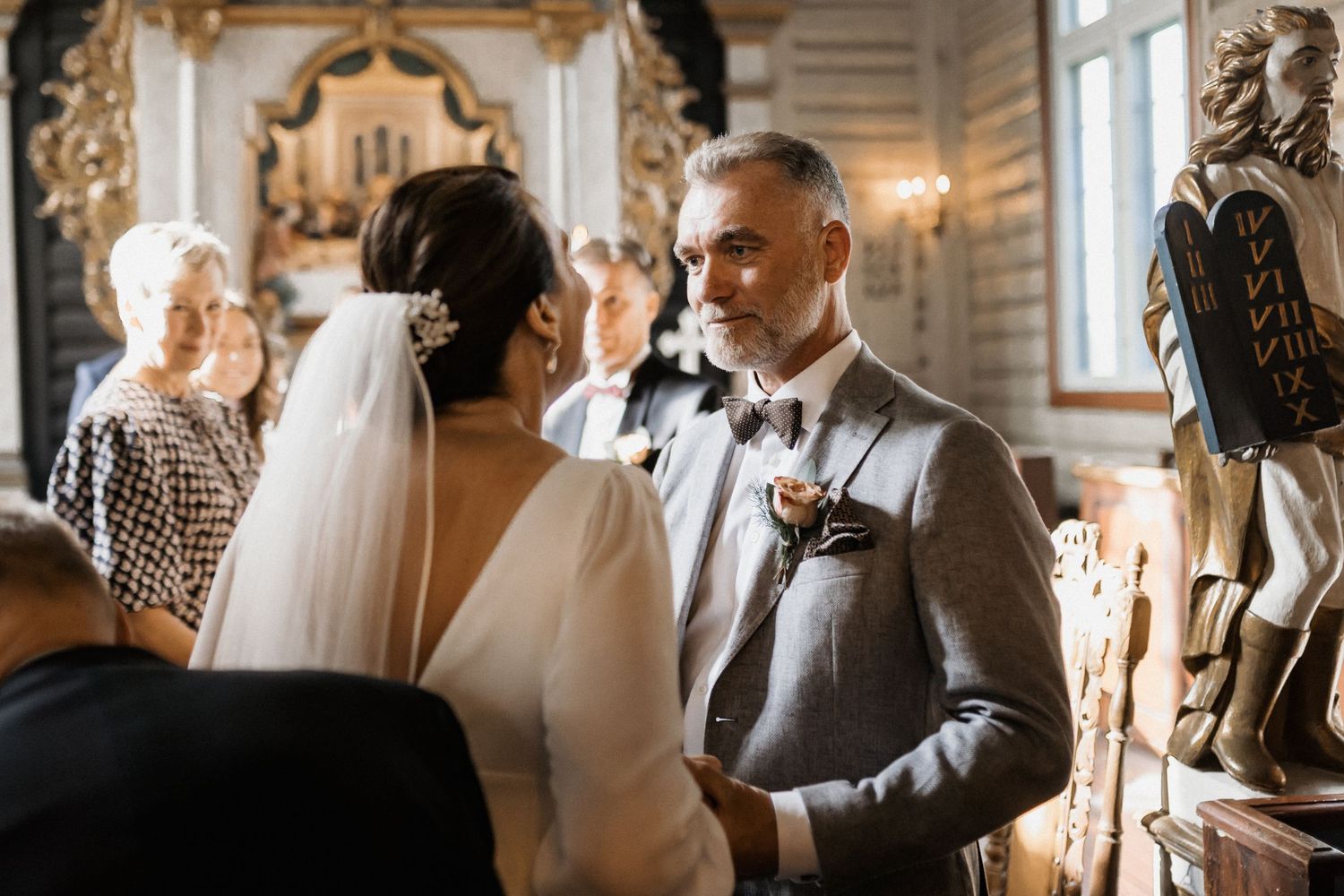 Wedding ceremony guests gathered in an elegant indoor venue with natural lighting.