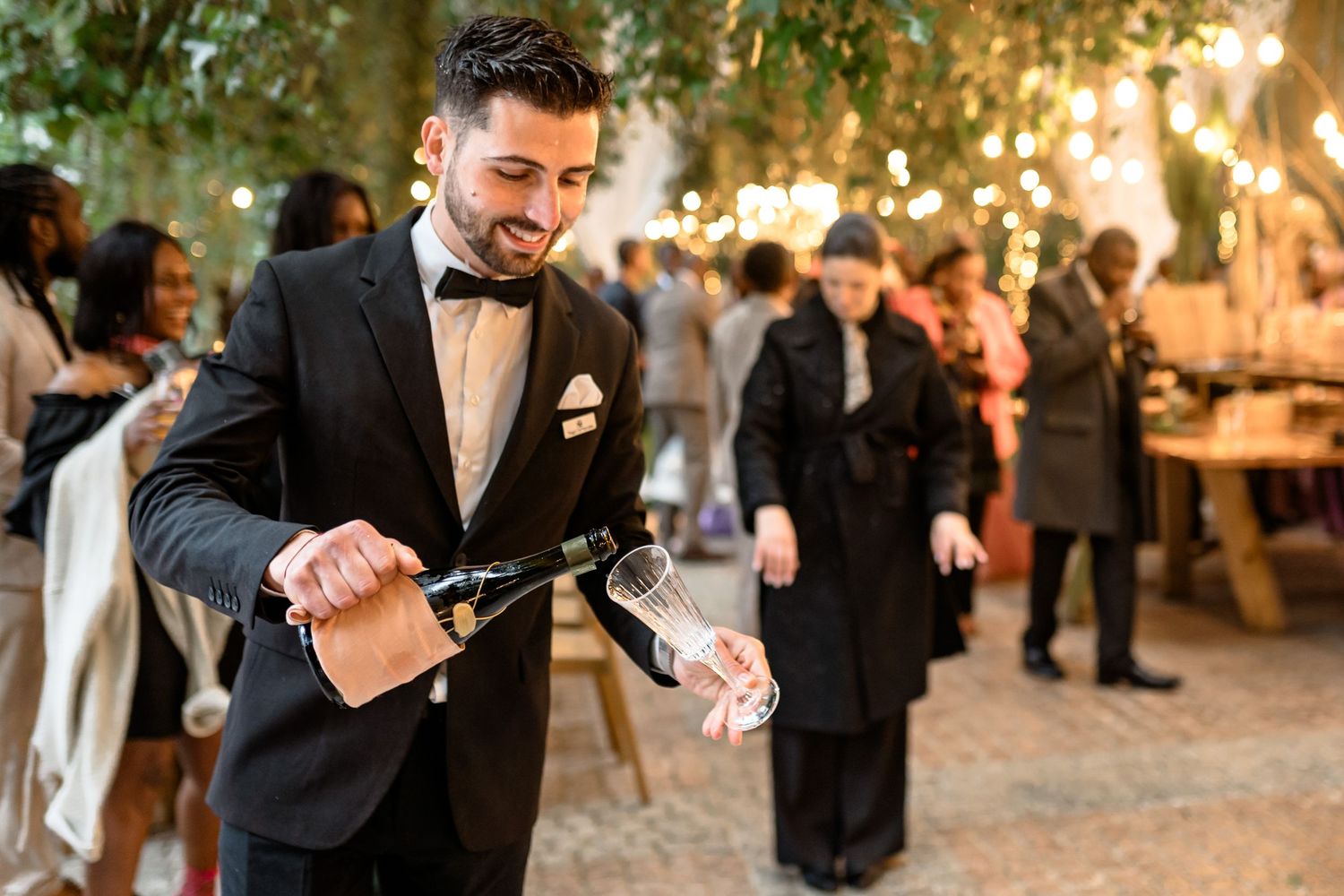 Elegant outdoor wedding reception with guests mingling under twinkling lights at dusk.
