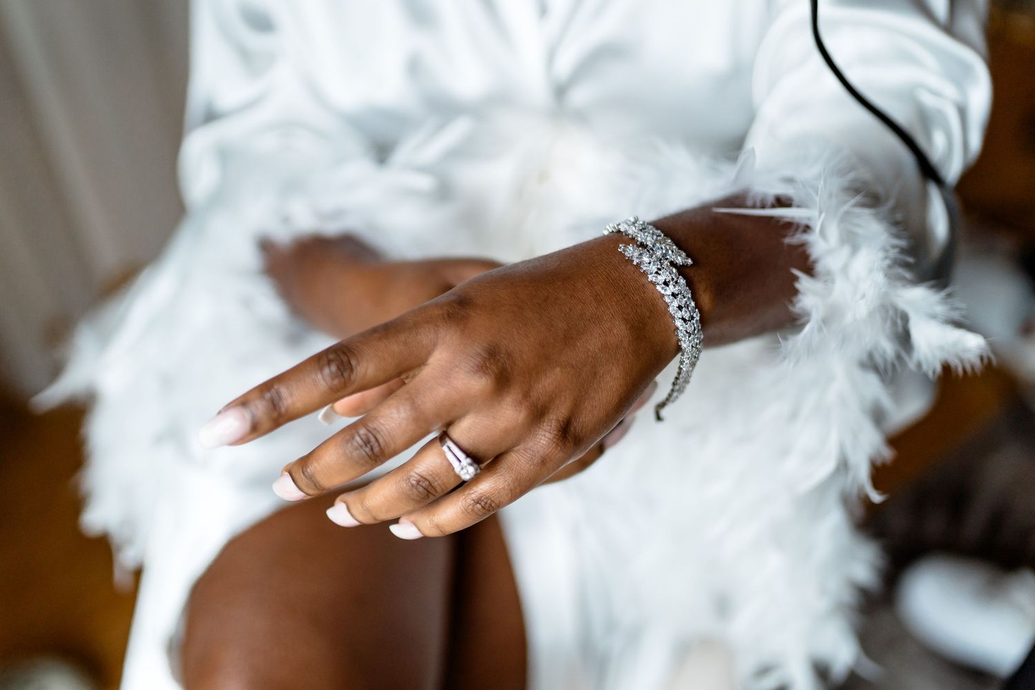 Close-up of an elegant hand wearing a diamond bracelet and ring against white feathery fabric.