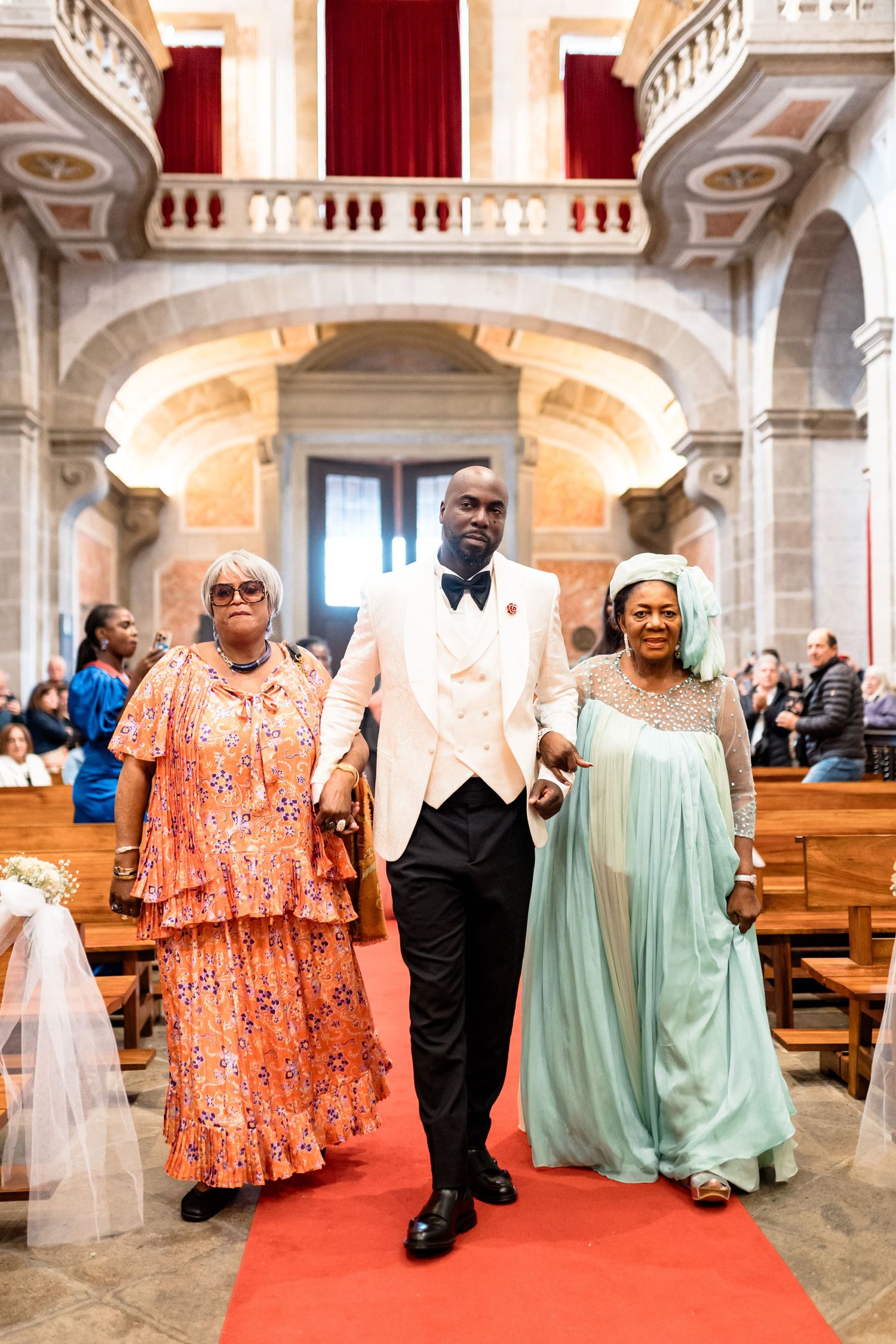 A wedding processional walking down a red carpet in an ornate church with grand architecture.