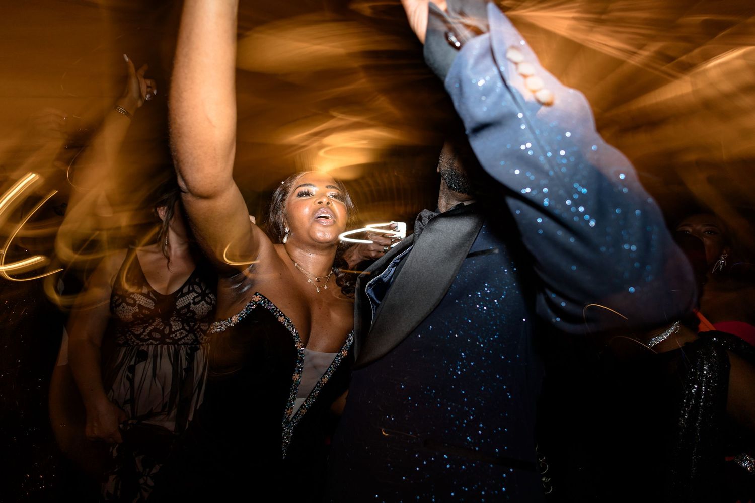 Dance floor scene at a wedding reception with dramatic amber lighting and silhouettes.