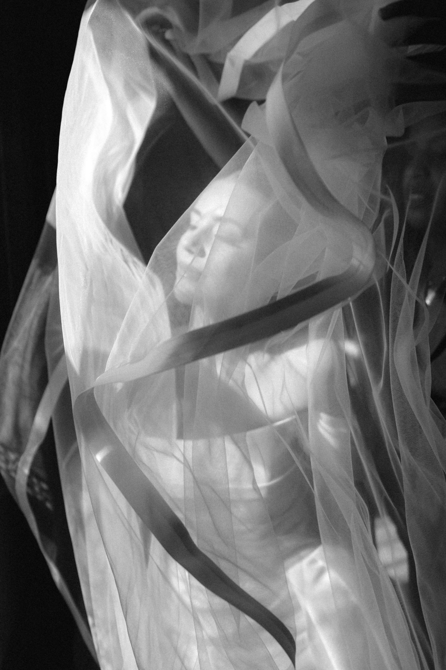 Black and white artistic photo of a woman draped in flowing sheer fabric, creating an ethereal and dreamlike composition.