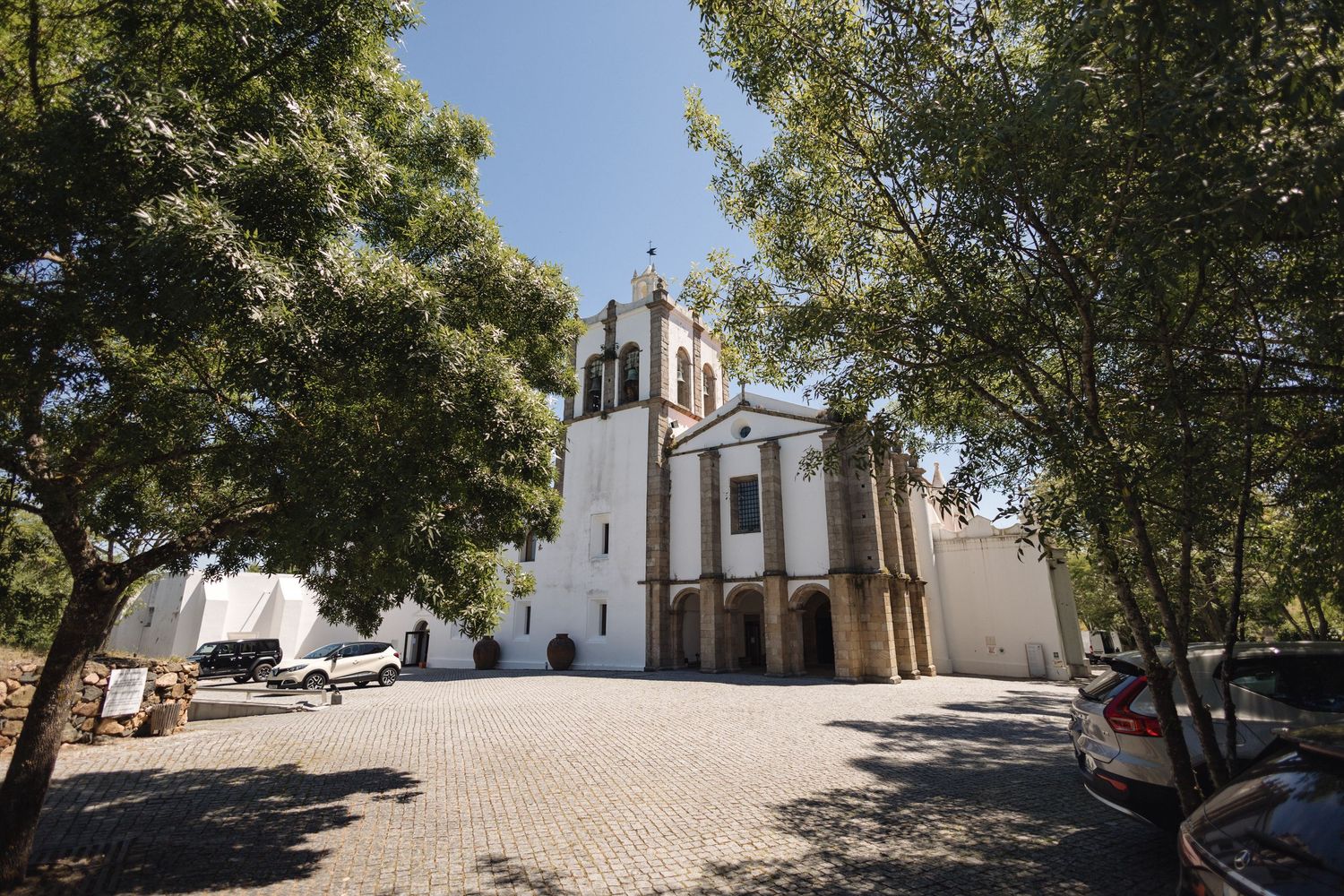 White church building and courtyard surrounded by trees on sunny day.