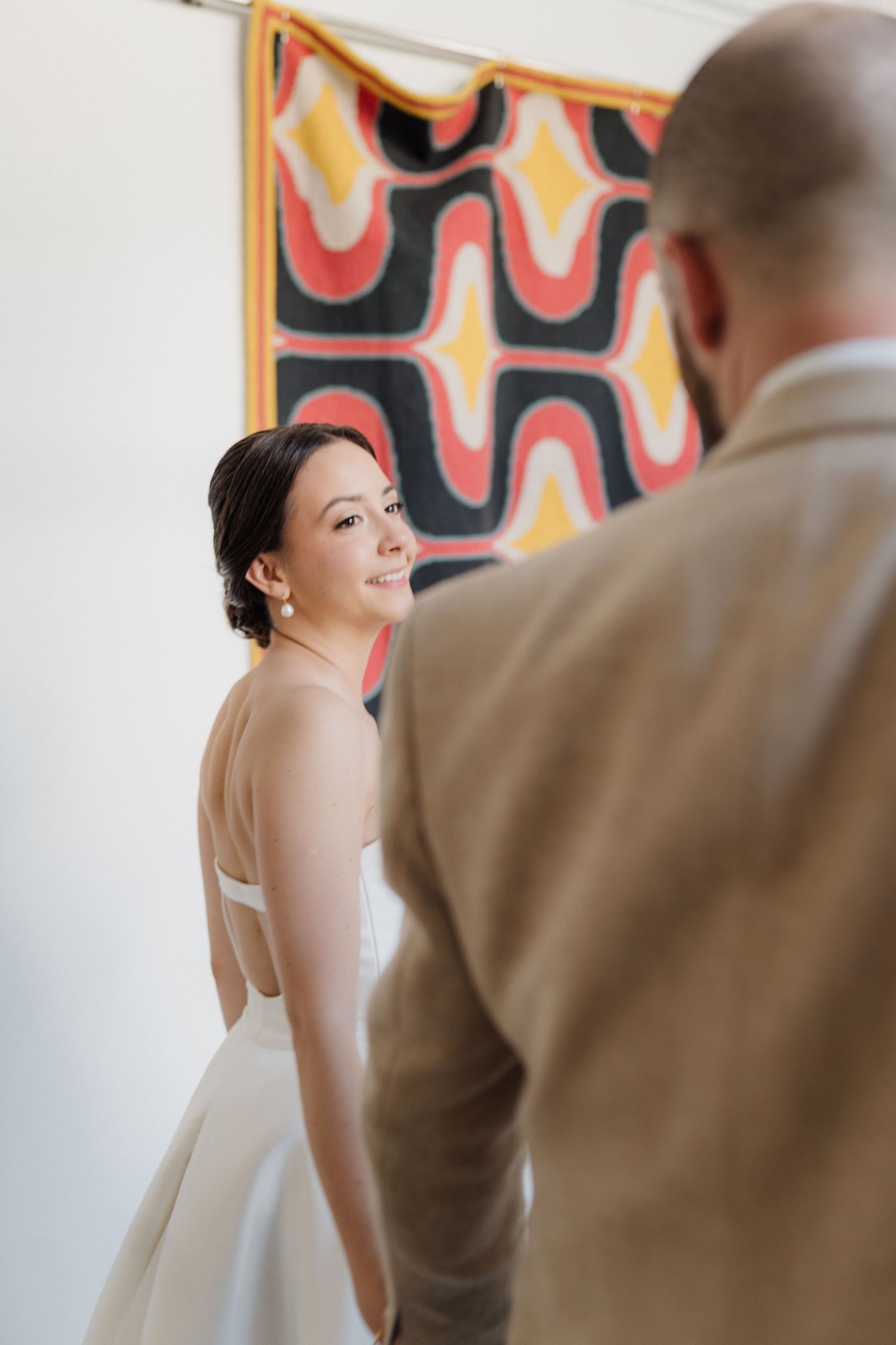 Bride in white dress poses against vibrant retro-patterned orange and yellow wall.