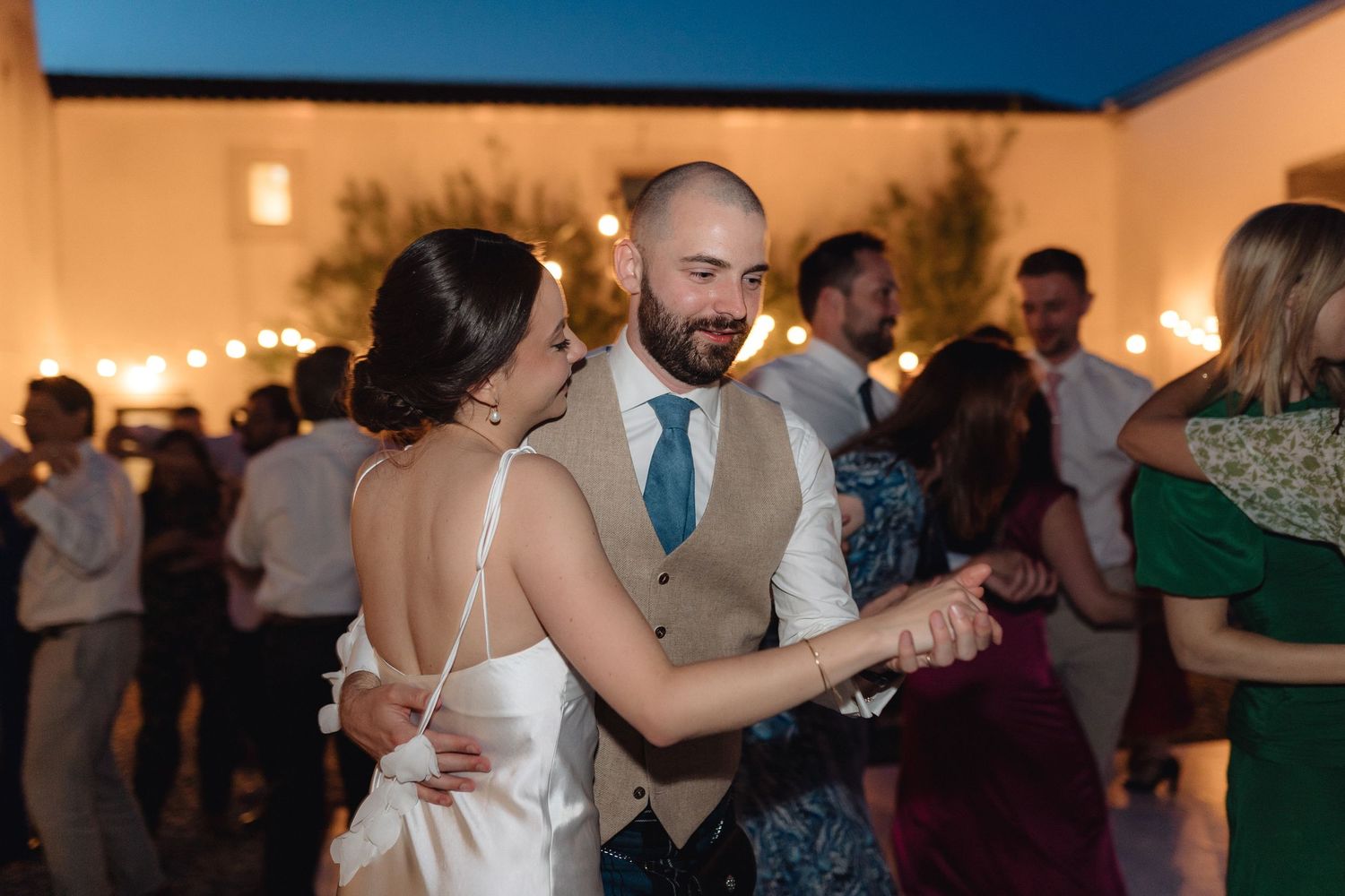 Wedding guests dancing and celebrating on a lively dance floor at an evening reception.